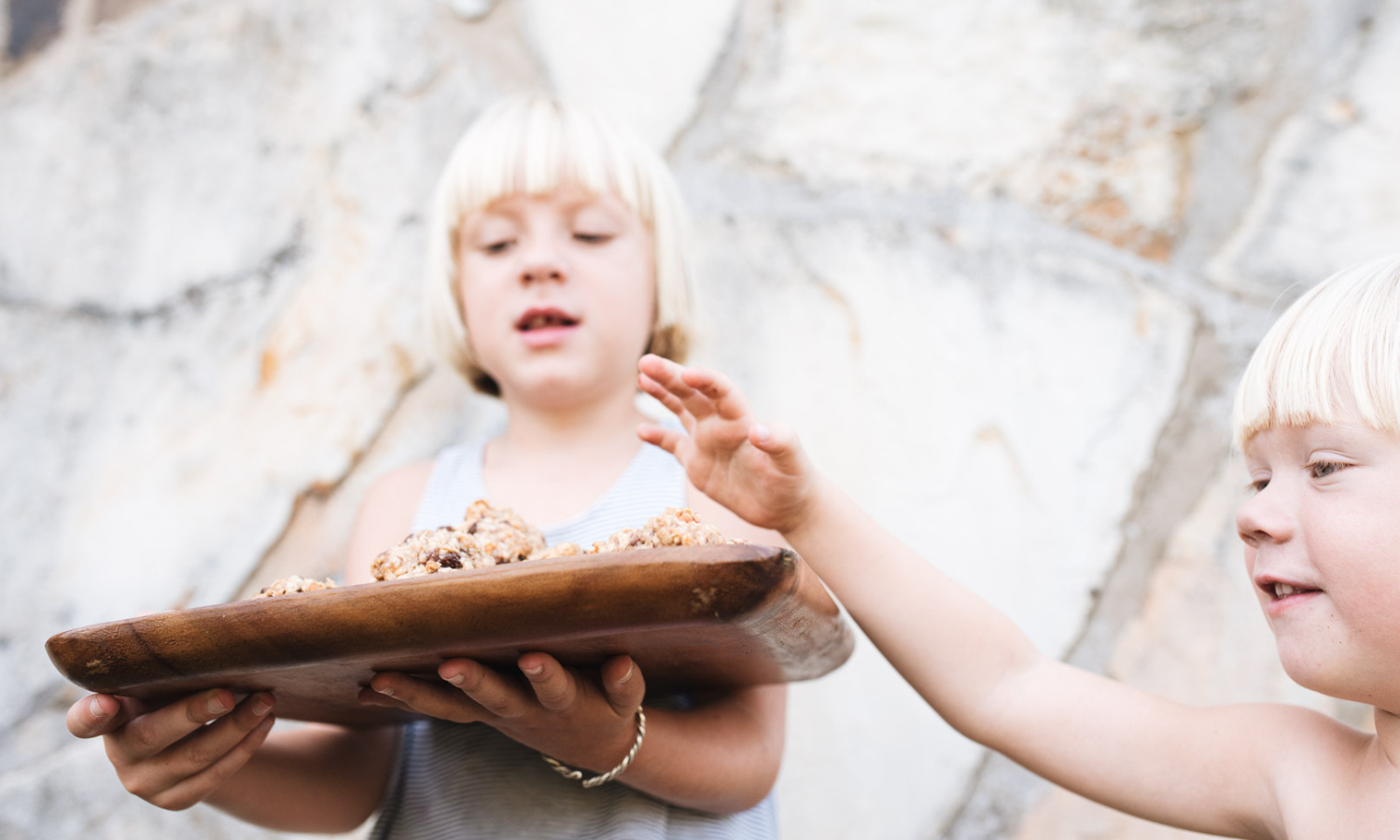 a little blonde girl with a tray of cookies and a little blonde boy trying to sneak one away