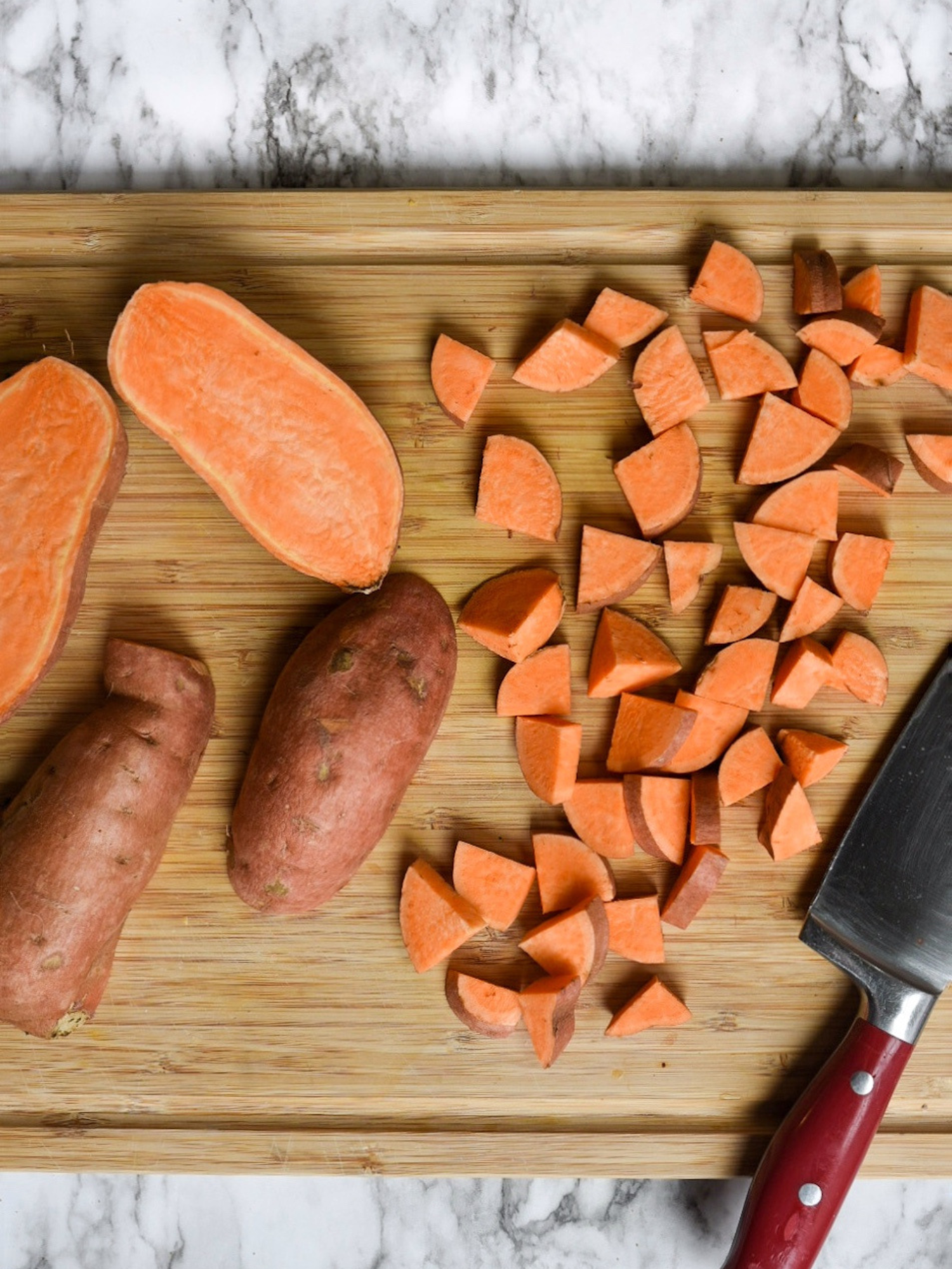 chopped sweet potatoes on a wooden cutting board with a knife