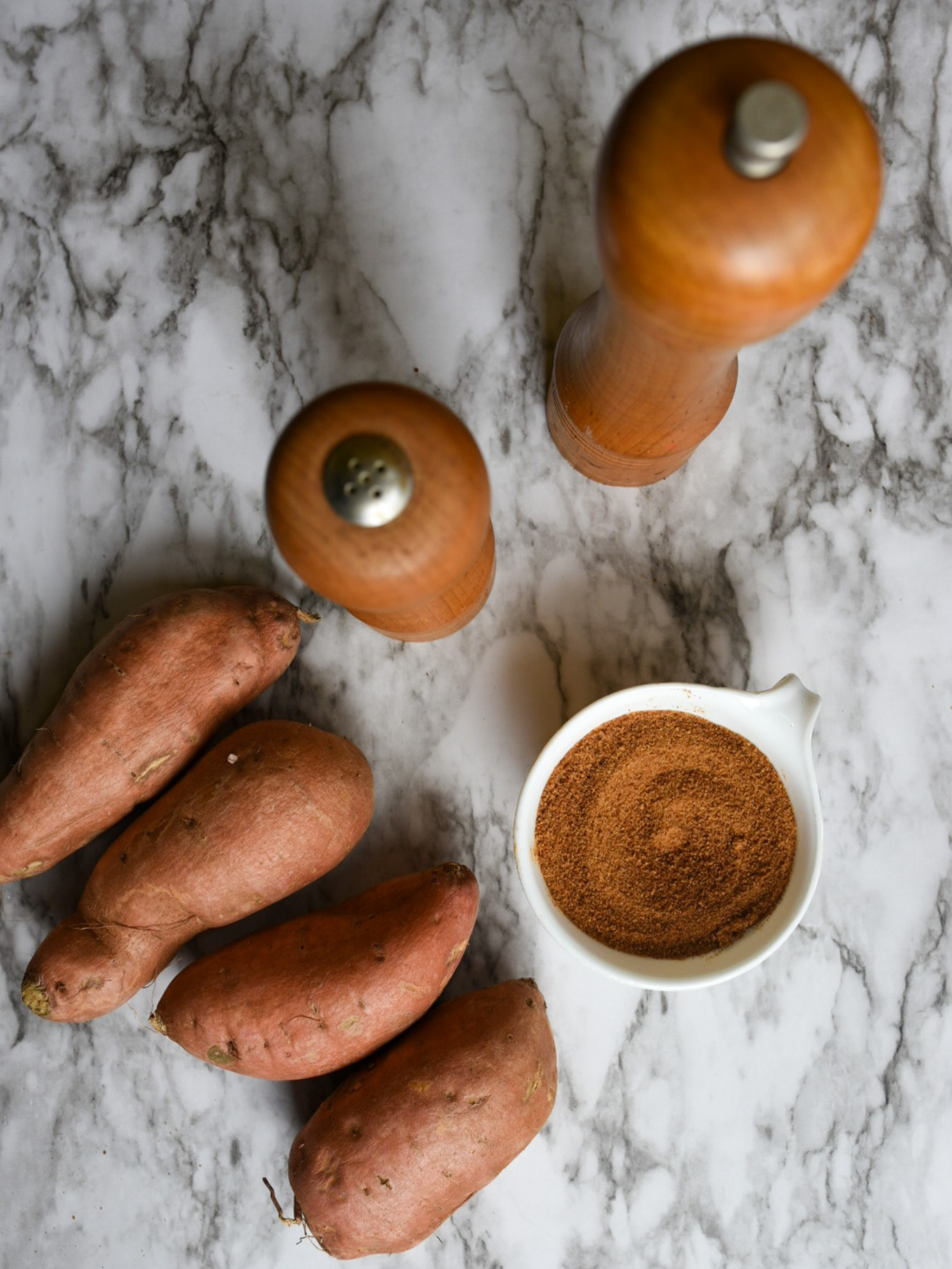 Ingredients for oil free roasted sweet potatoes: 4 sweet potatoes, salt and pepper shaker and coconut sugar on a marble countertop