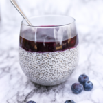 a glass cup filled with vanilla chia seed pudding and topped with homemade blueberry sauce