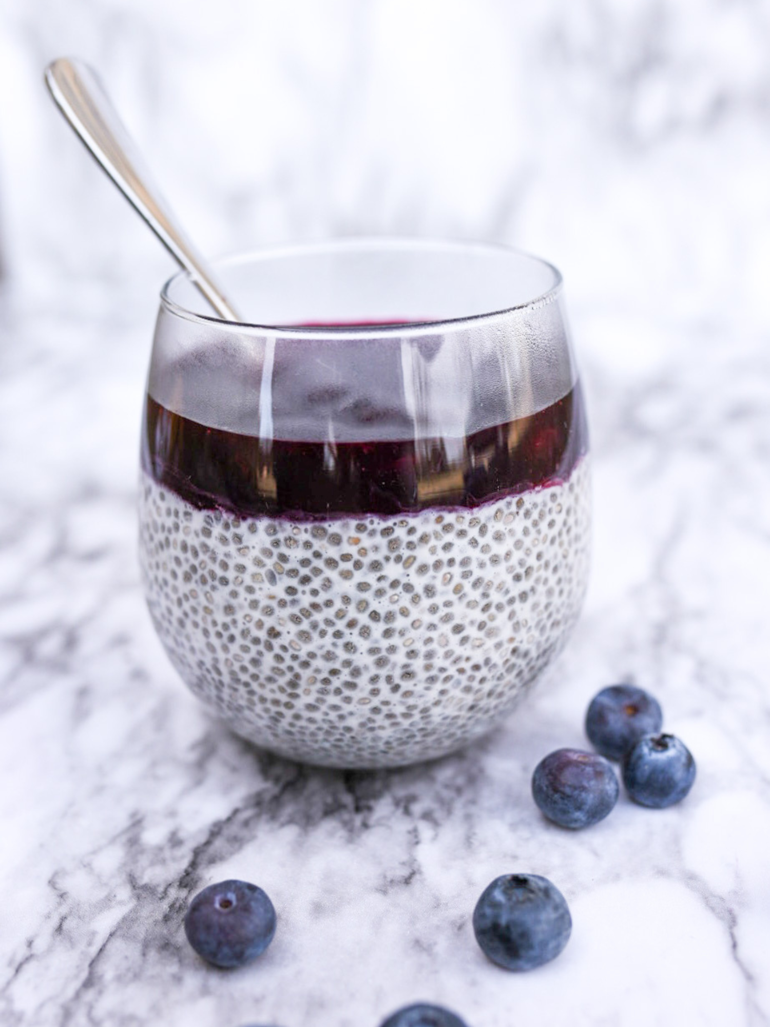 a glass cup filled with vanilla chia seed pudding and topped with homemade blueberry sauce