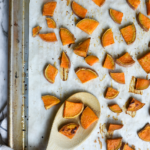 a baking sheet with parchment paper with roasted sweet potatoes cubes and a wooden spoon