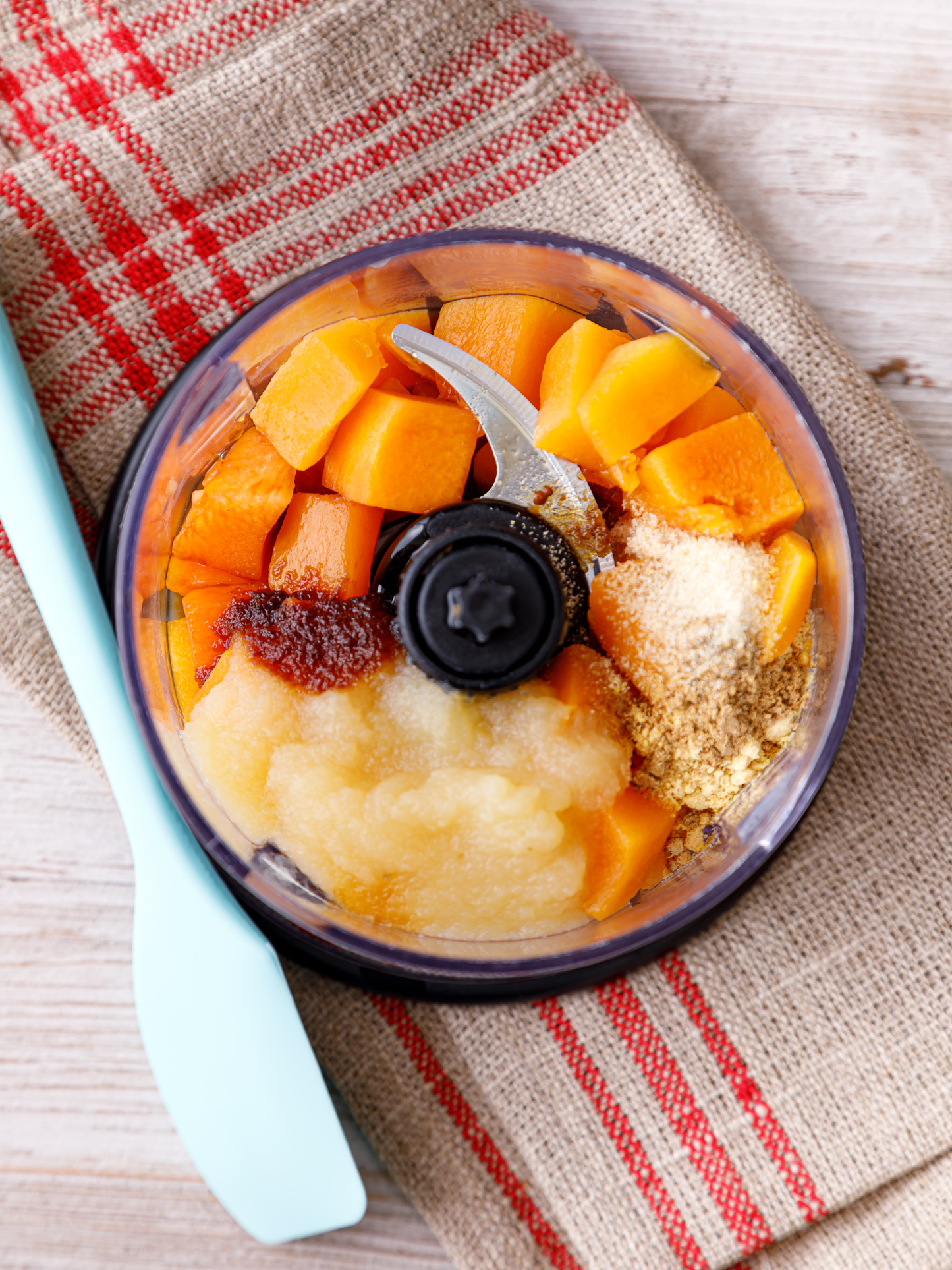 a blender with vegetable ingredients next to a spoon