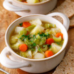 two white bowls filled with irish cabbage soup on table with a silver spoon