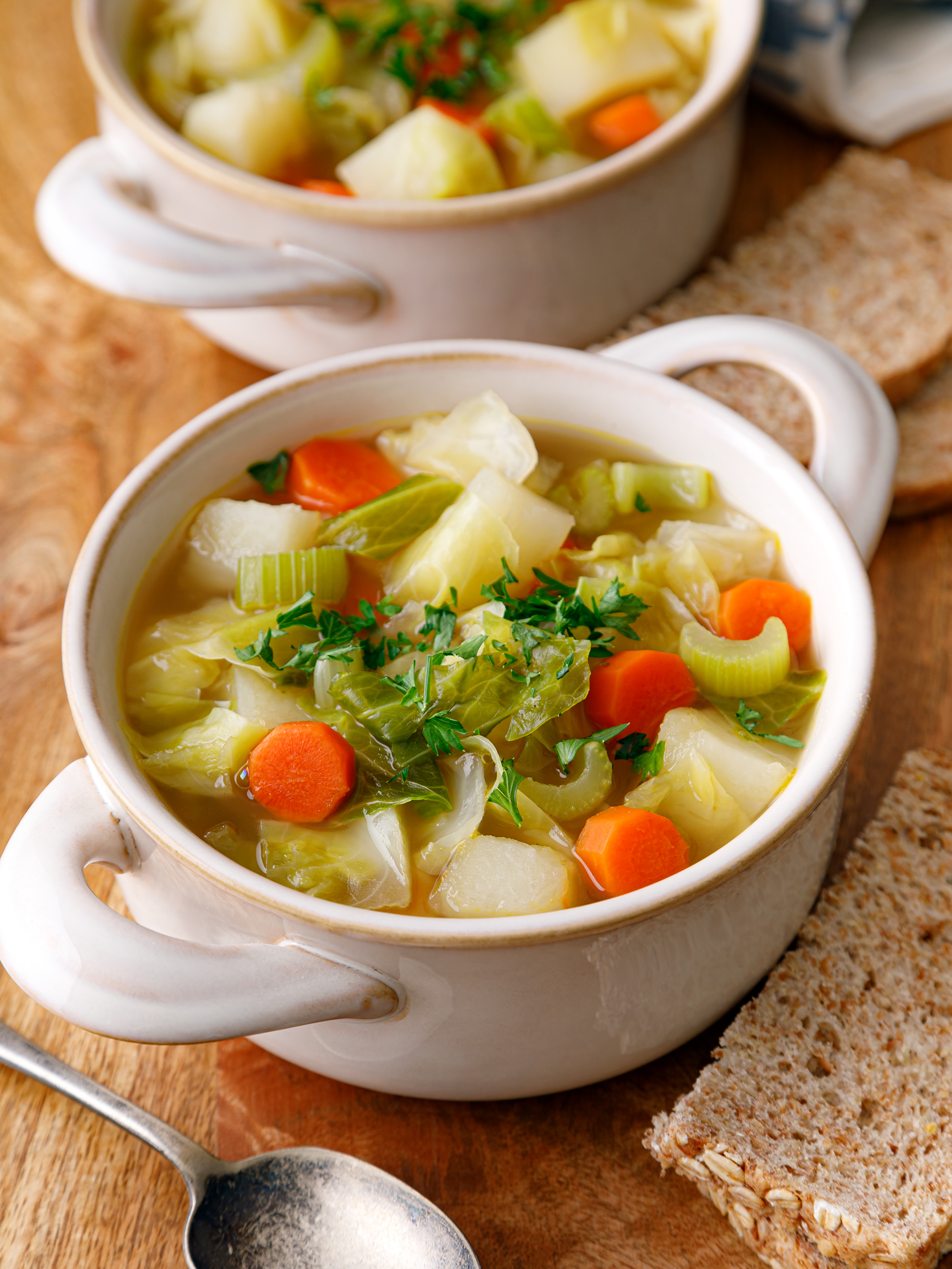 two white bowls filled with irish cabbage soup on table with a silver spoon