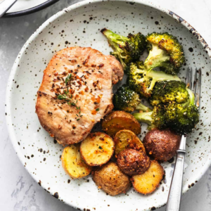 a white speckled plate with roasted pork chop, potatoes and brocooli and a silver fork 