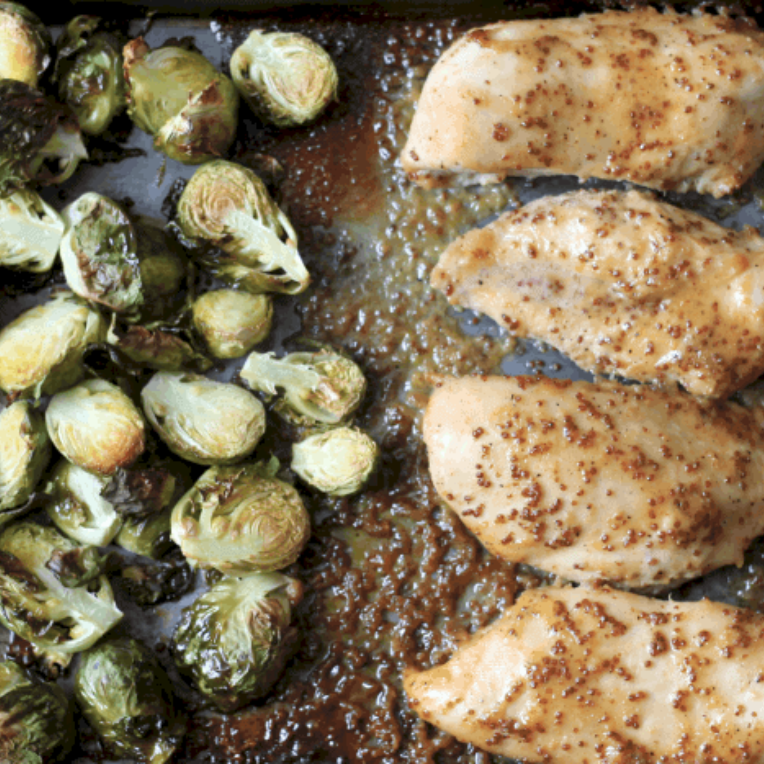 A baking sheet with baked chicken breast on one side and roasted brussel sprouts on the other side all covered in a honey mustard sauce