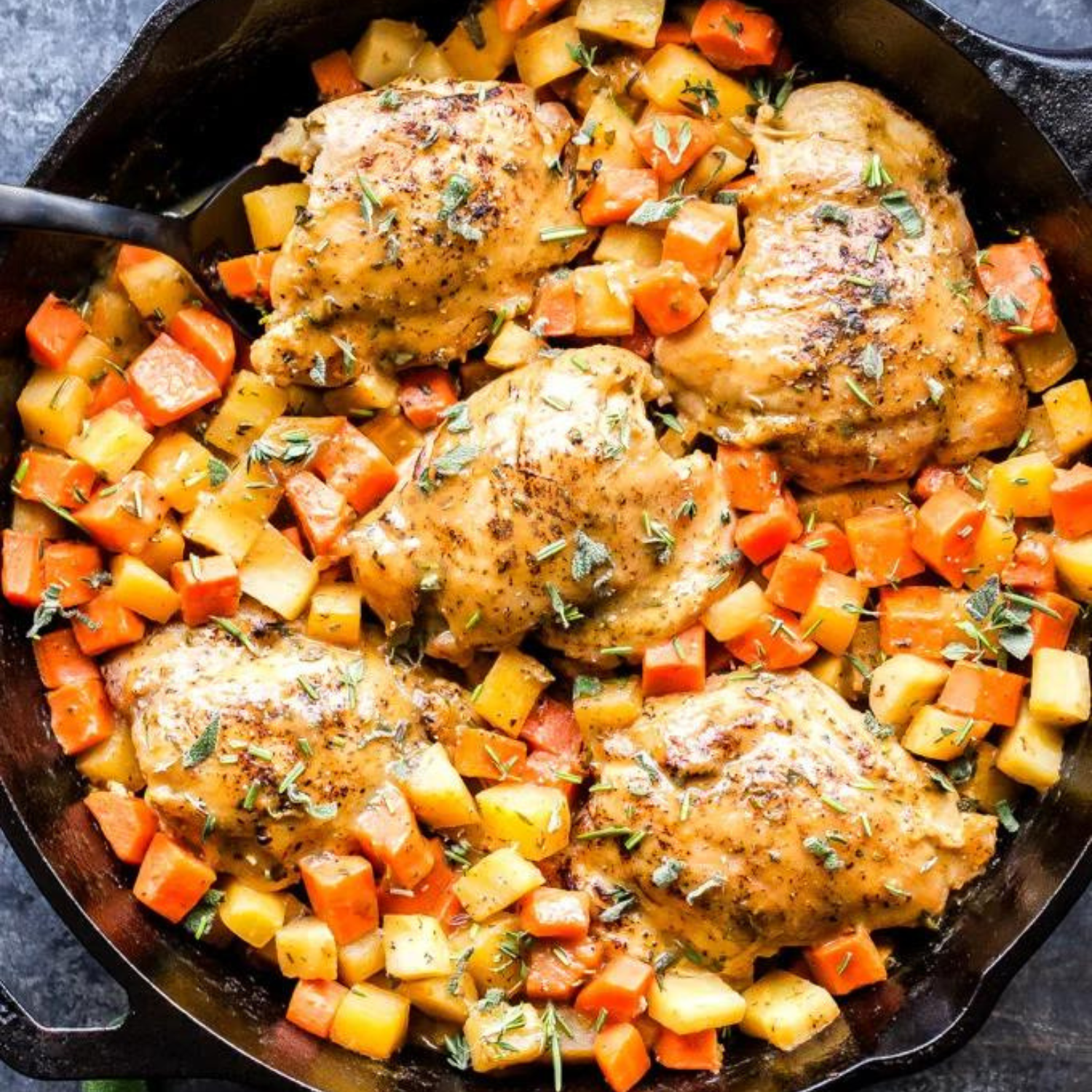 a cast iron skillet with roasted cubed root vegetables with baked chicken thighs in an apricot jam glaze