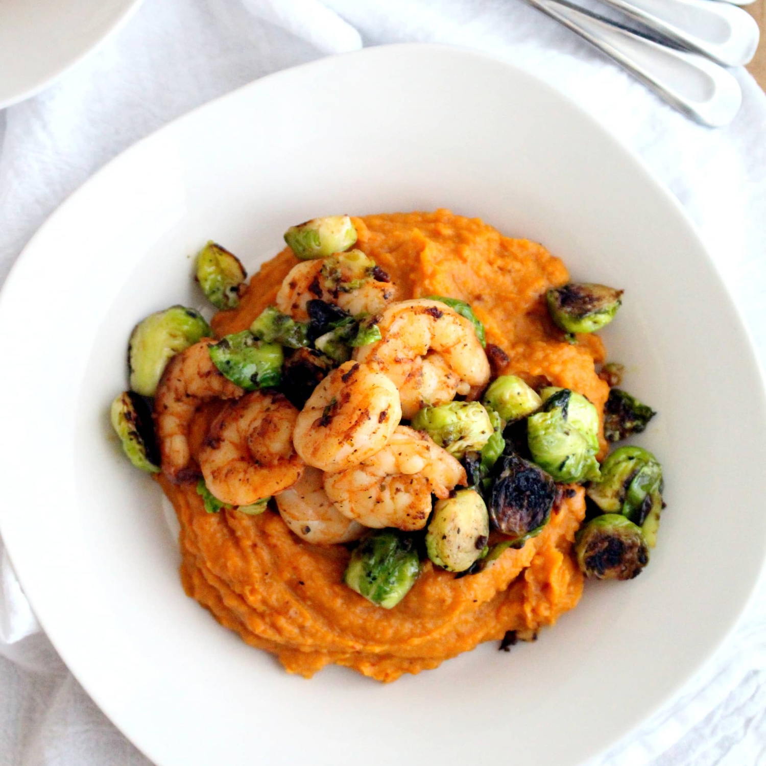 a white bowl layered with a sweet potato mash topped with roasted brussel sprouts and sauteed shrimp