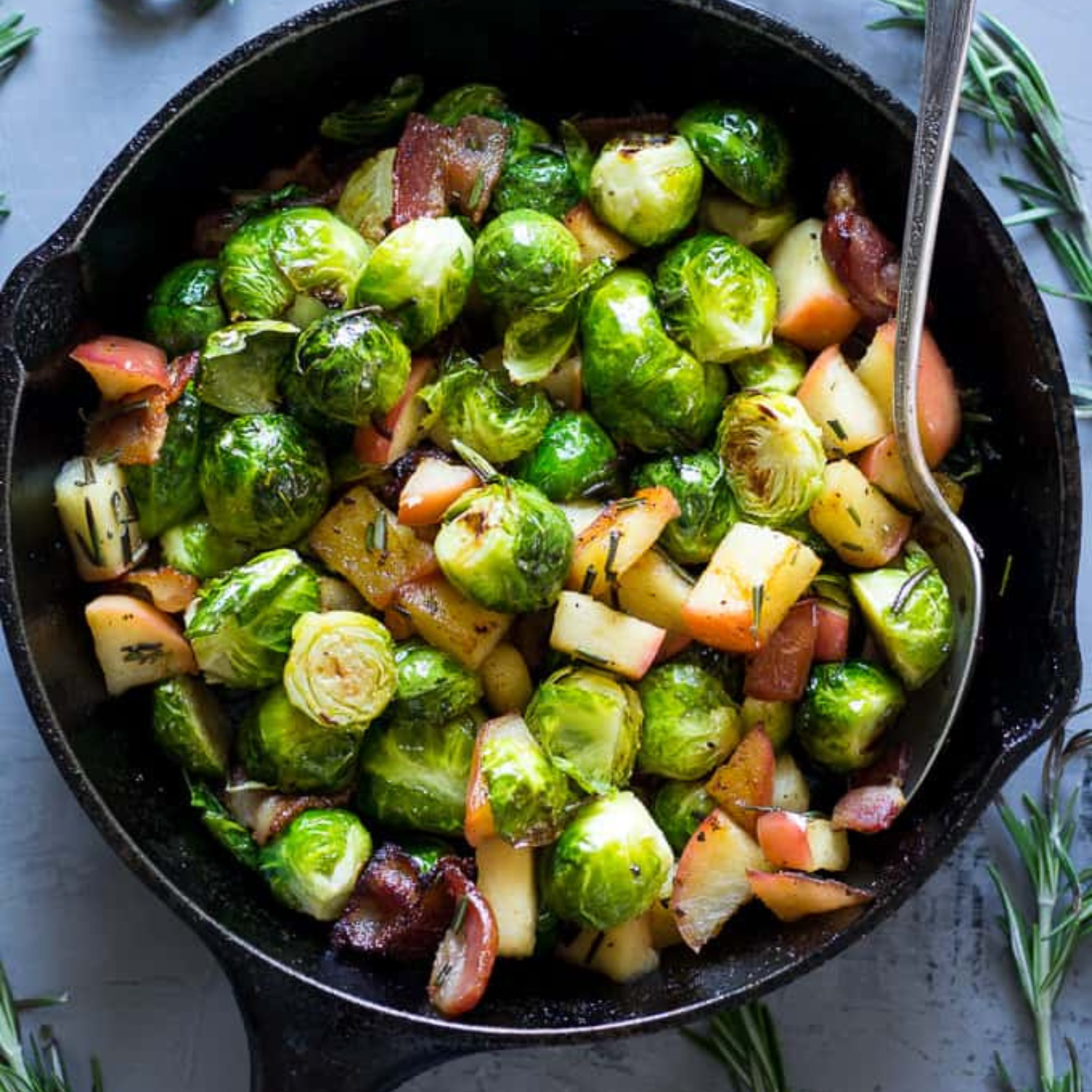 an iron skillet with roasted brussel sprouts, bacon and apples, with a silver spoon