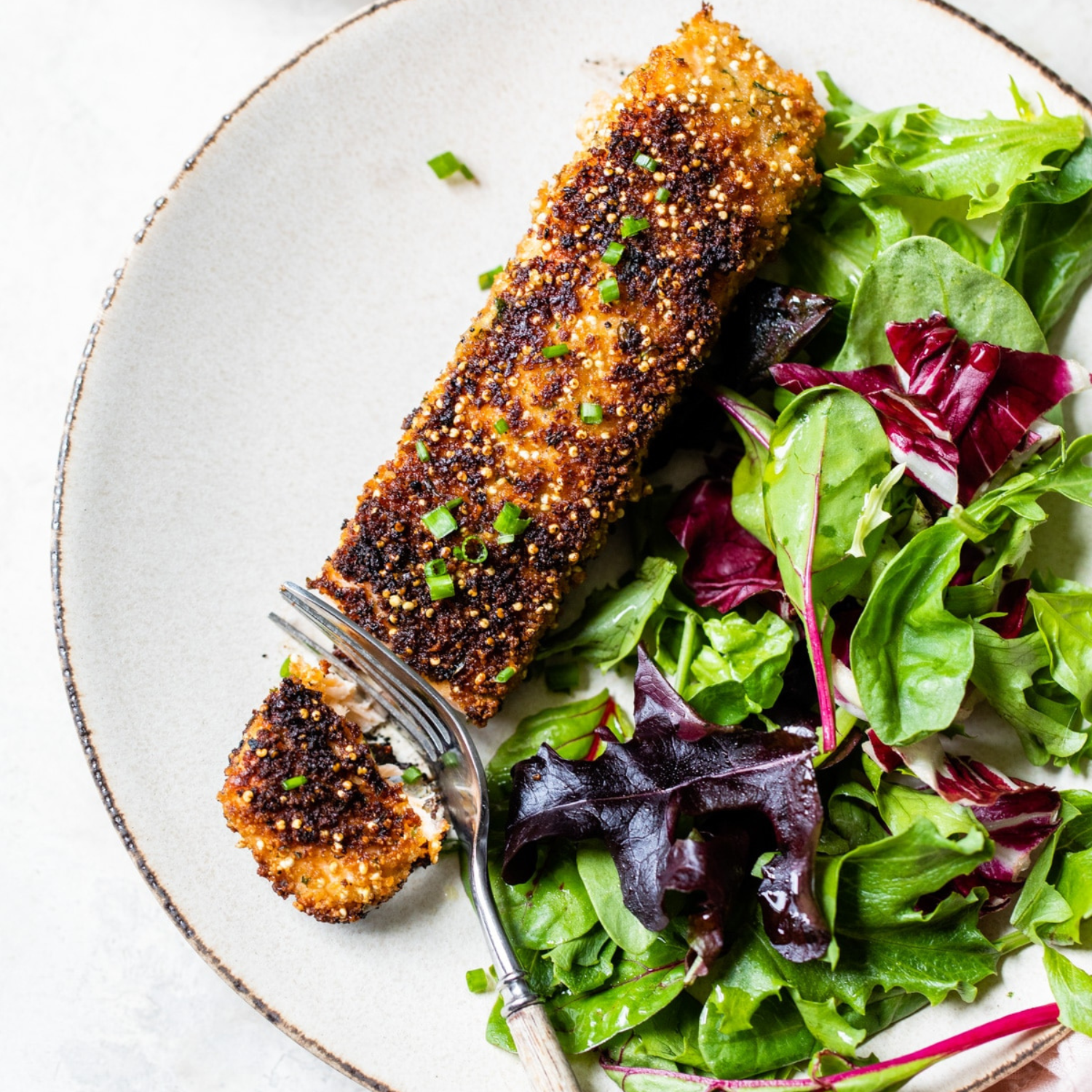 a piece of quinoa crusted salmon on a white plate with a side salad