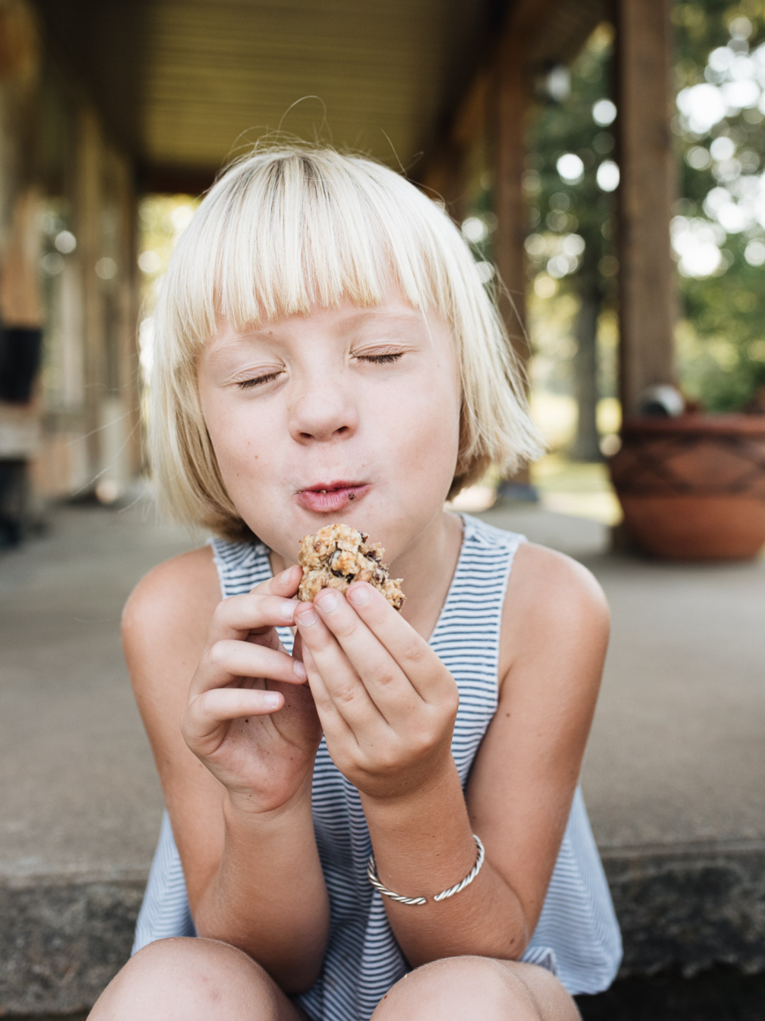 a little blonde girl on a front stoop enjoying a gluten free dairy free cookie