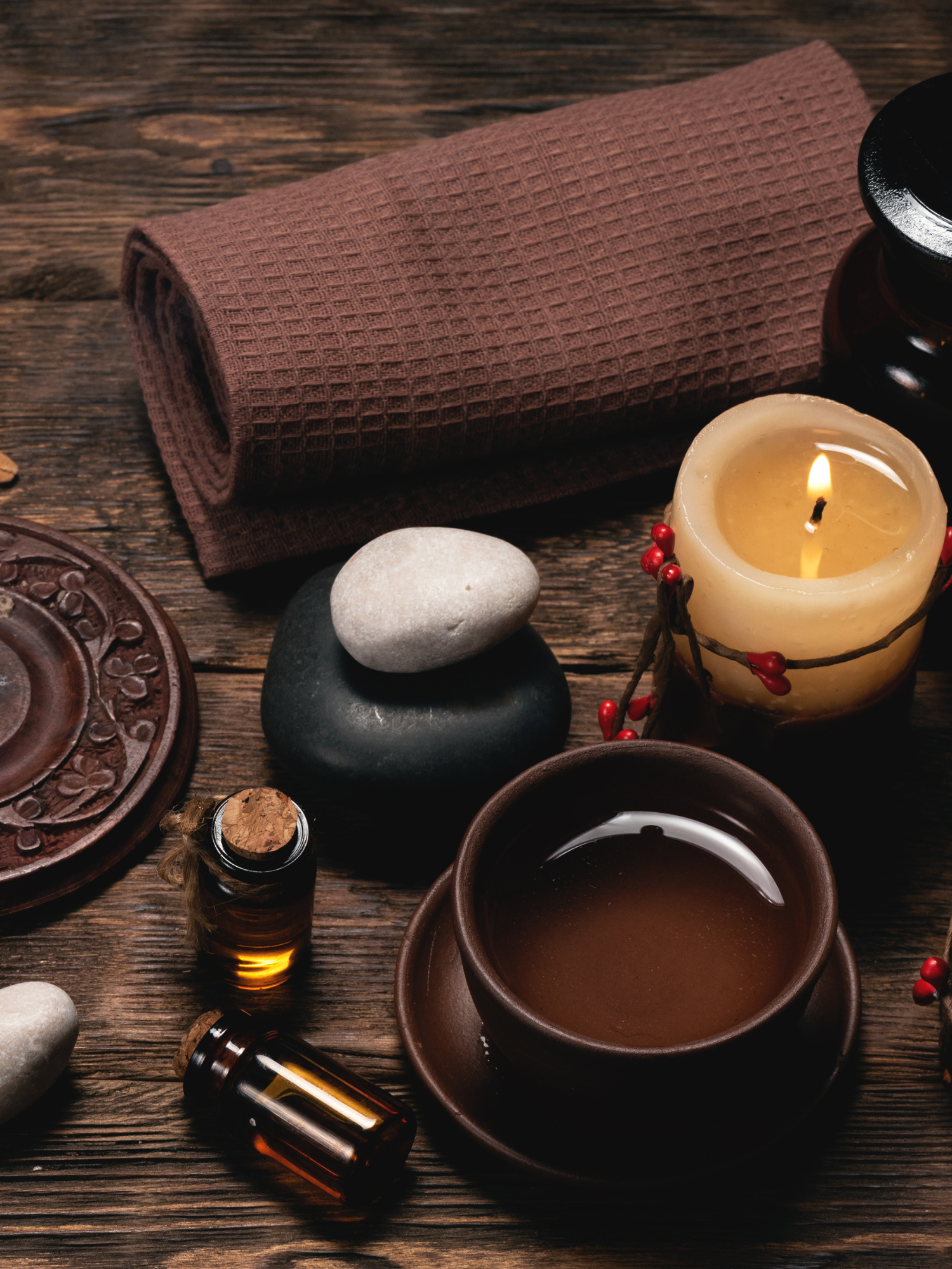 a lit candle, teacup, and brown glass bottles on a wooden table