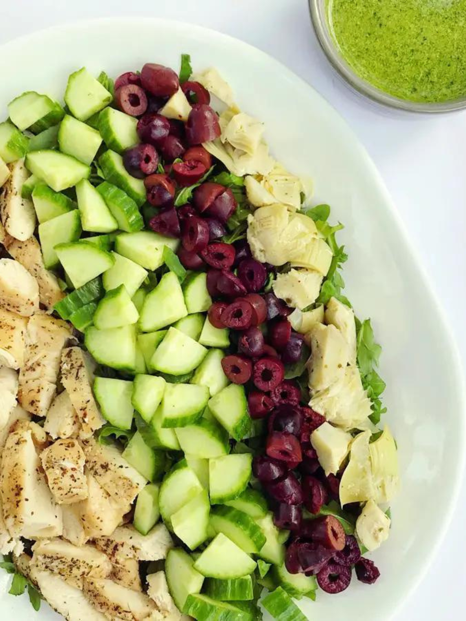 arugula chopped salad topped with artichoke hearts, olives, chicken, cucumbers, and a side of basil dressing