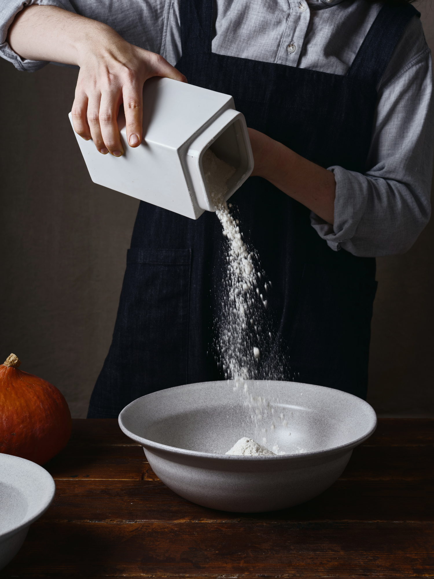 a woman in a black apron pouring flour into a bowl