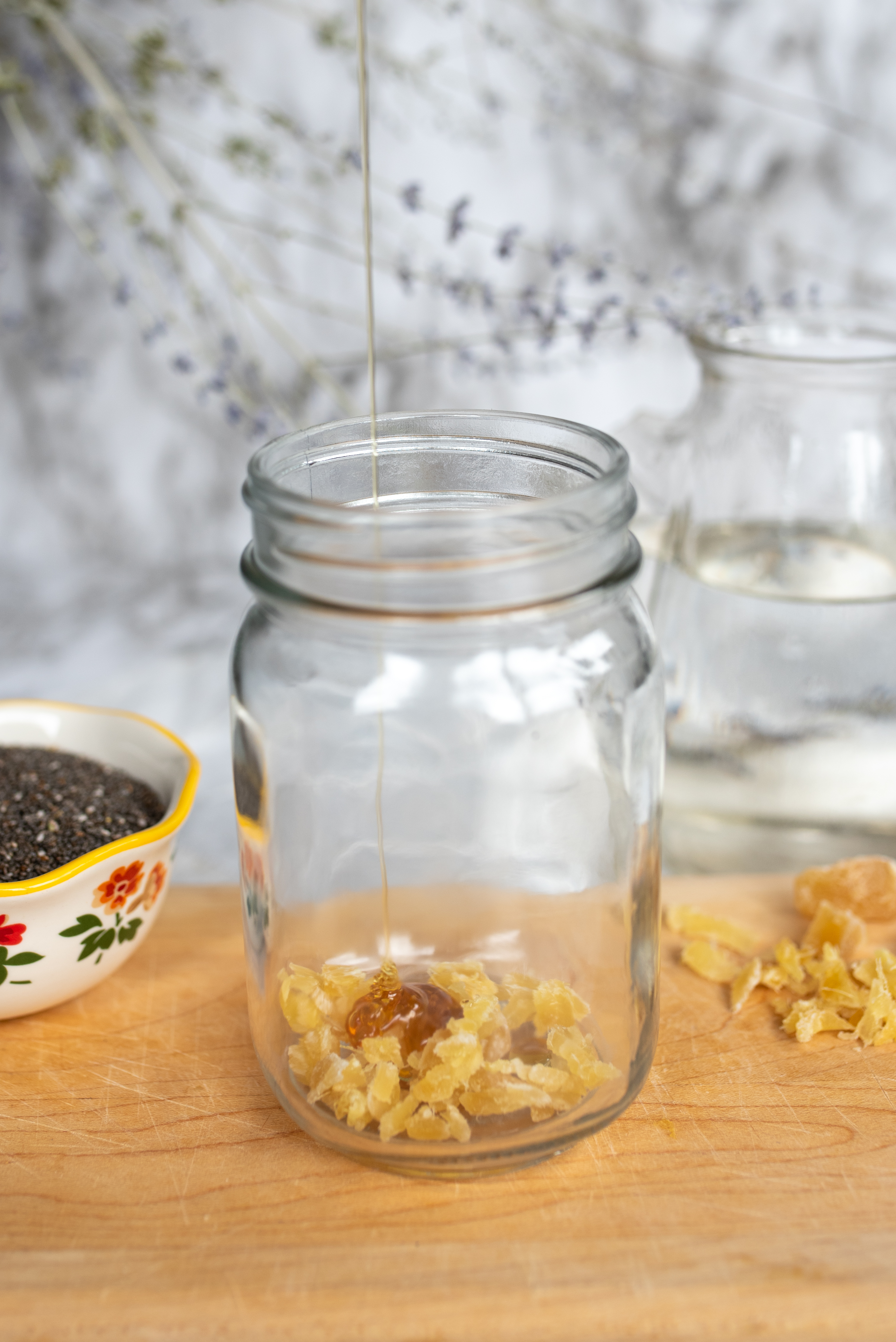 a glass with pieces of fruit and honey sits on a wooden cutting board