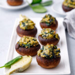 5 mushrooms stuffed with spinach and artichoke feeling on a white plate sitting on a white table