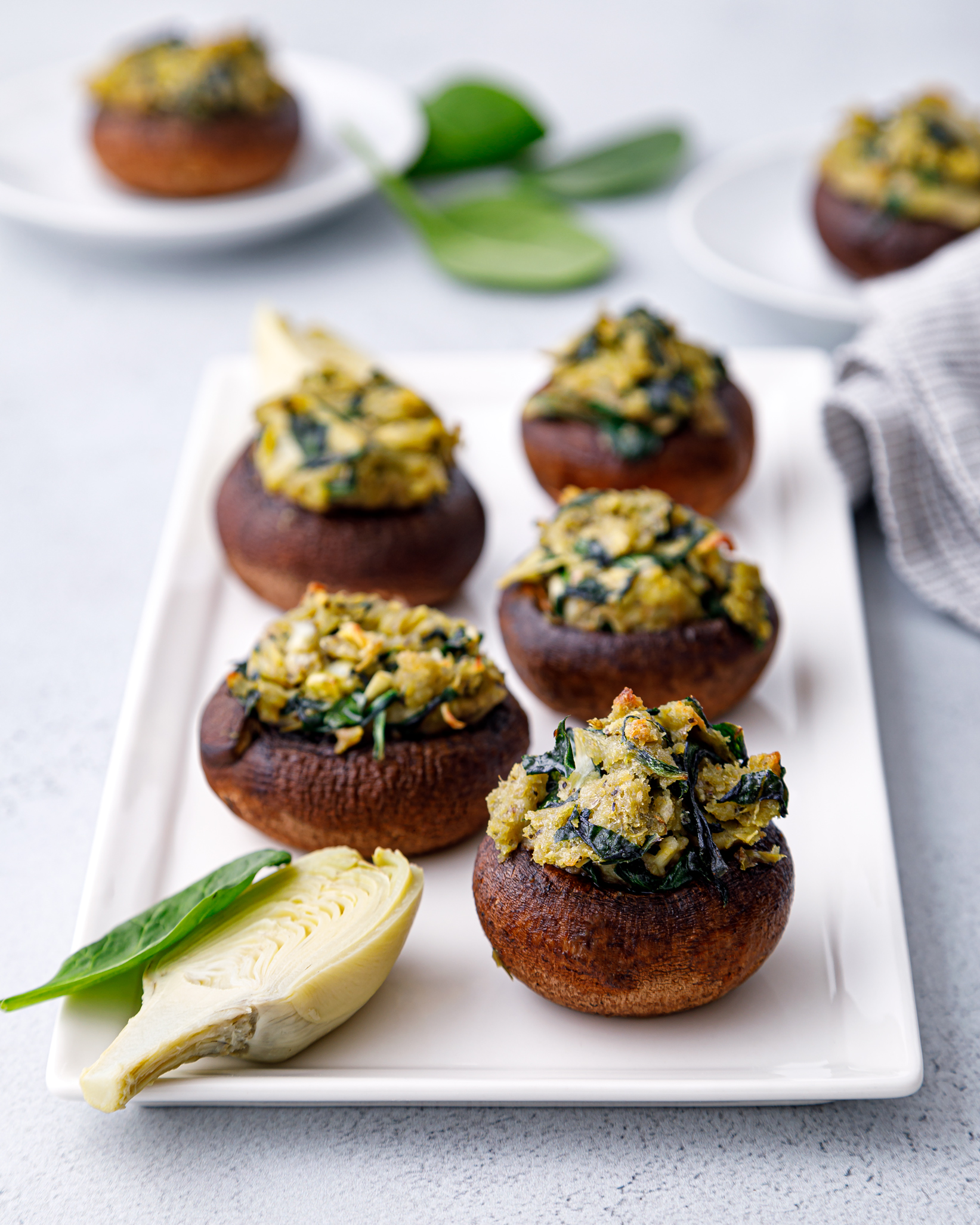 5 mushrooms stuffed with spinach and artichoke feeling on a white plate sitting on a white table