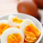 hard boiled eggs cut in half with yellow yolks showing in a white plate with brown hard boiled eggs in the background