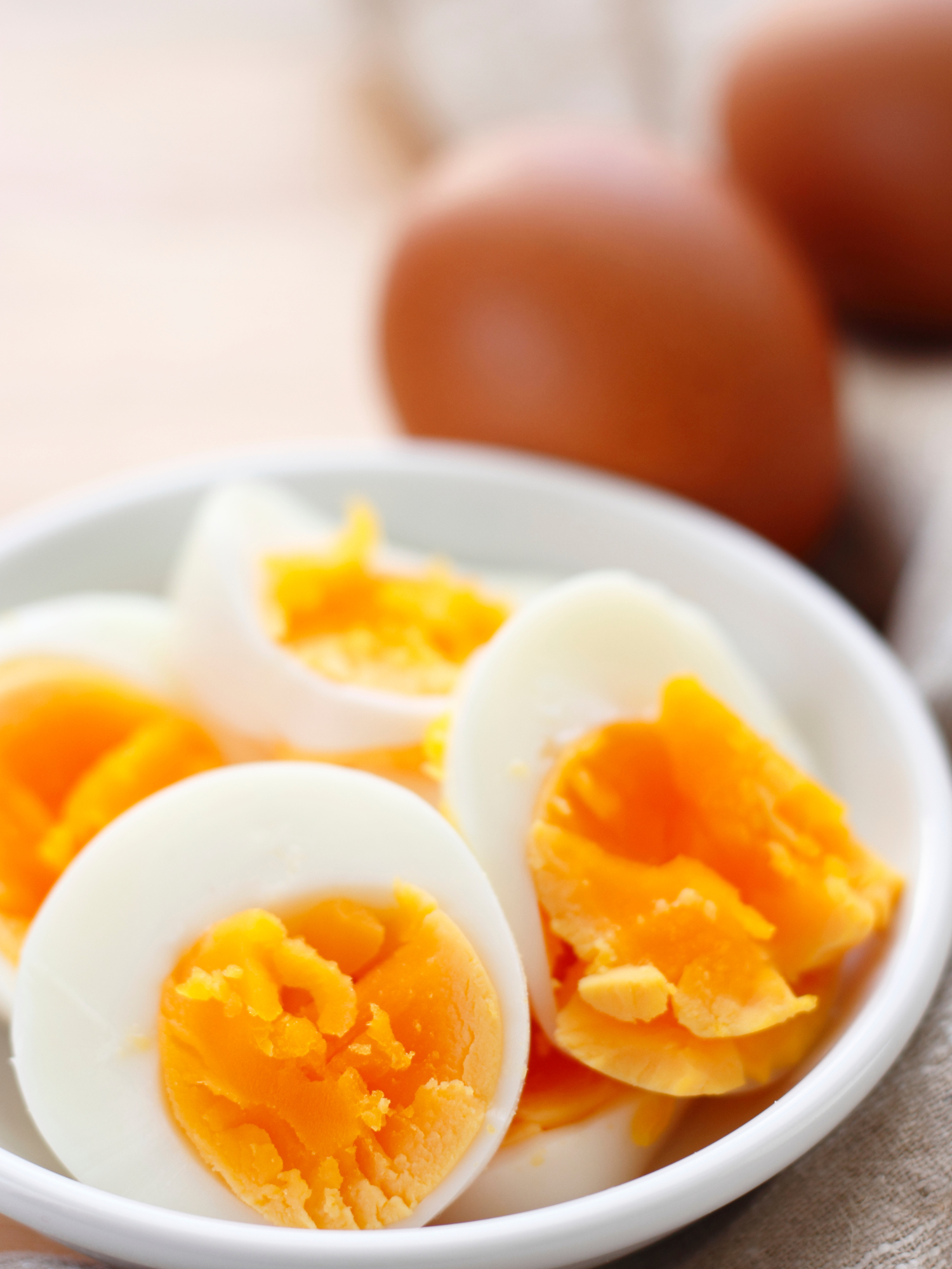 hard boiled eggs cut in half with yellow yolks showing in a white plate with brown hard boiled eggs in the background