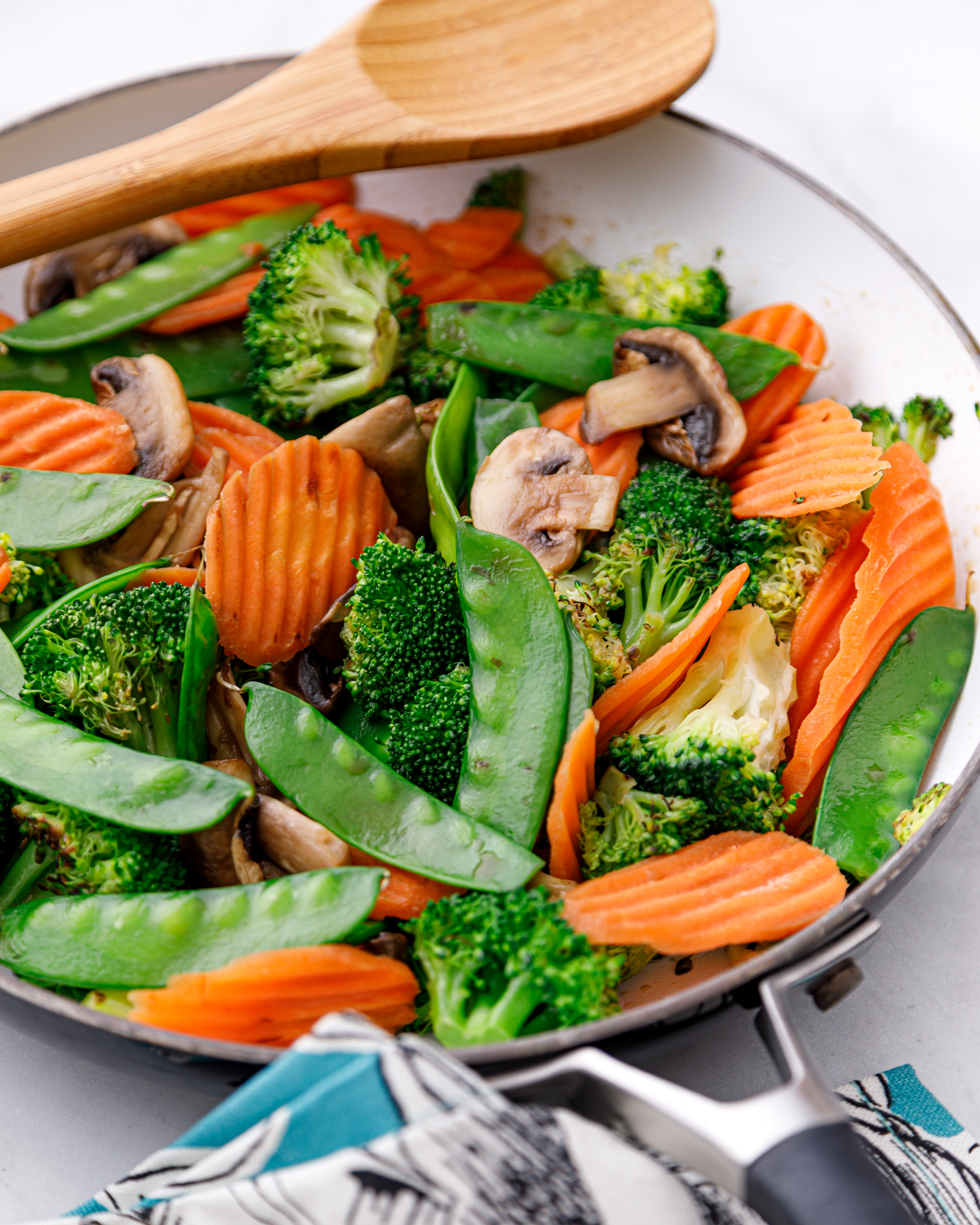 colorful chopped vegetables in a skillet with a wooden spoon resting on it