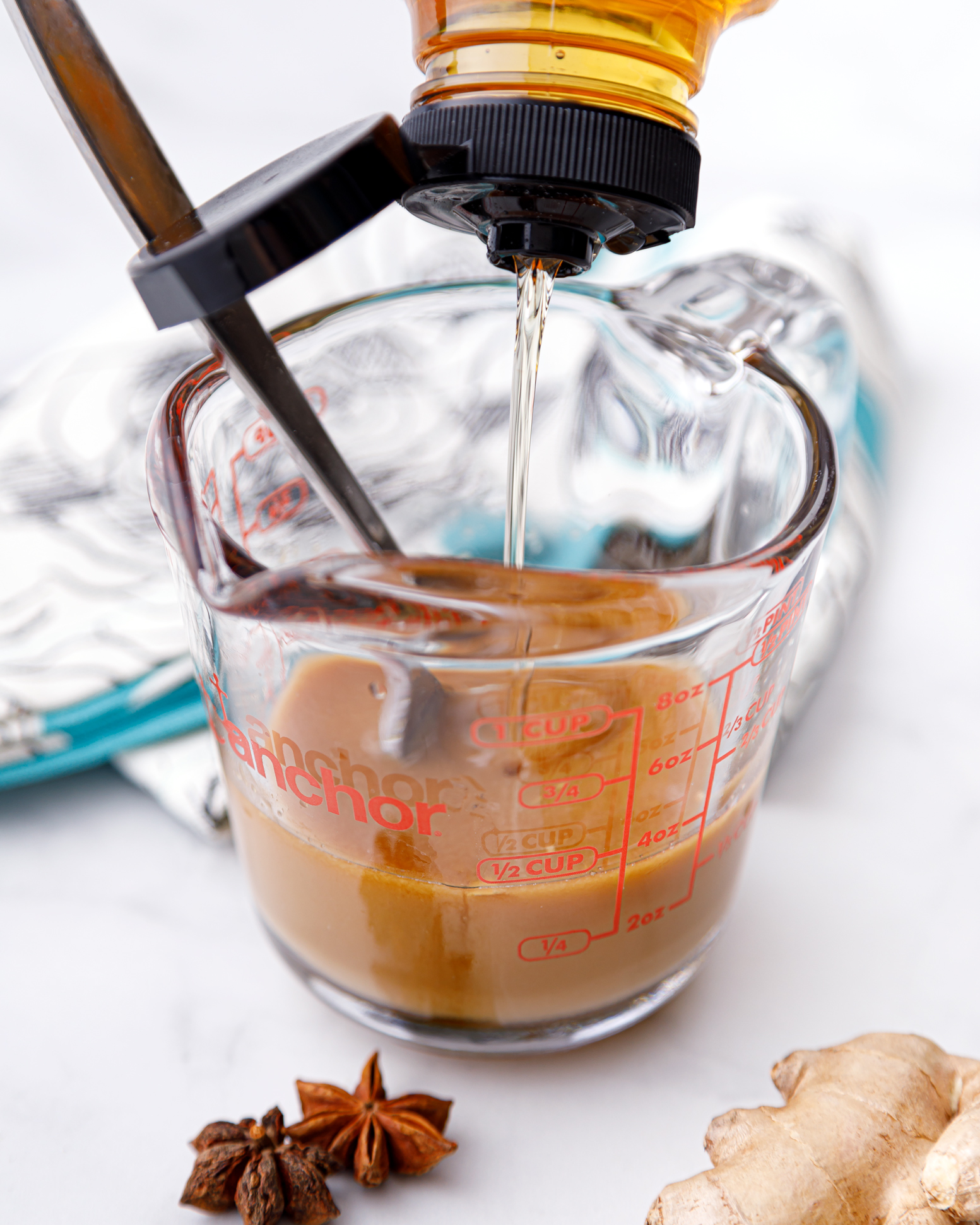 measuring glass of brown liquid and honey being dripped into the mixture