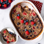 a white casserole dish of quinoa breakfst bake topped with fresh blueberries and rasberries next to a bowl of fresh blueberries and raspberries