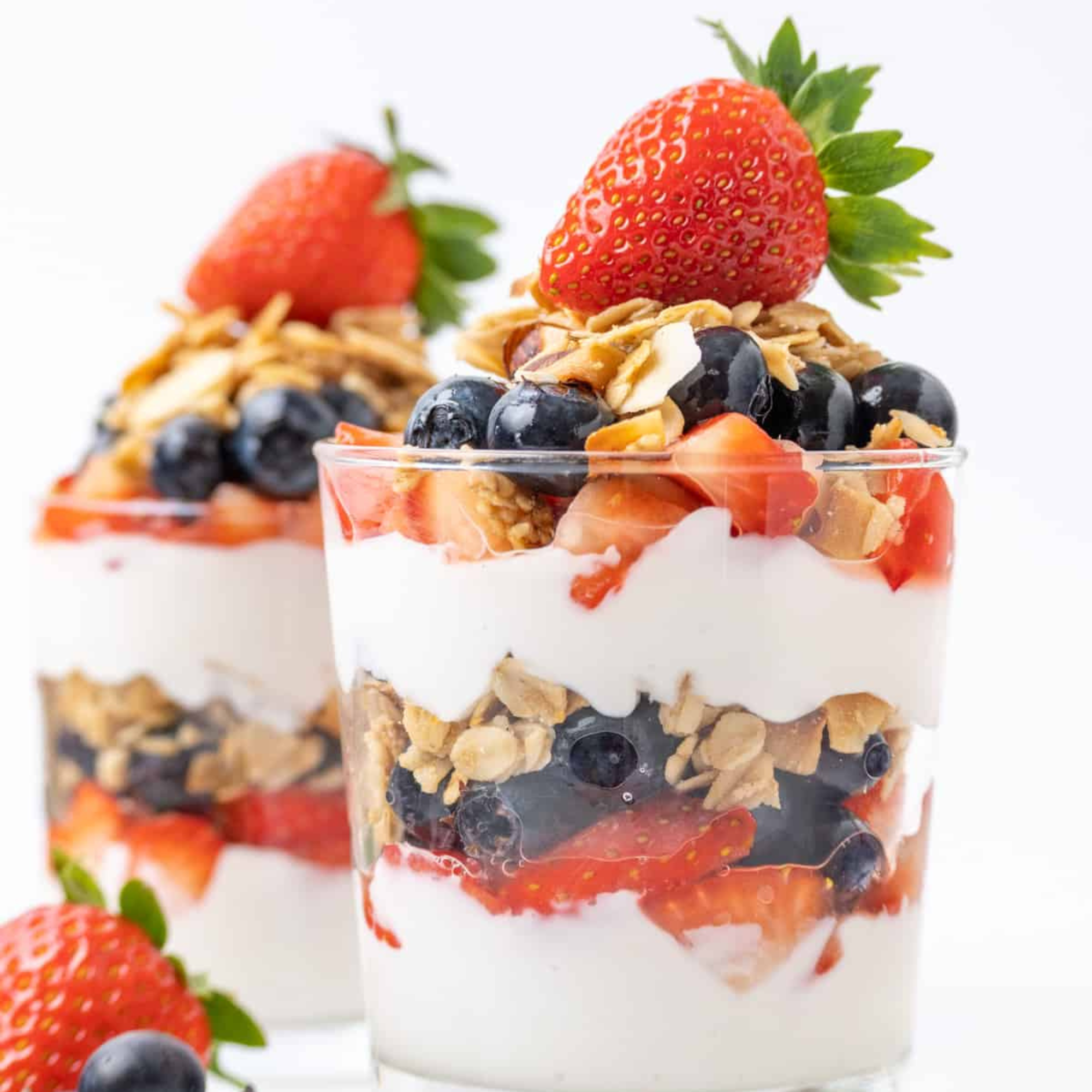two vegan yogurt parfaits topped with vegan granola and strawberries
