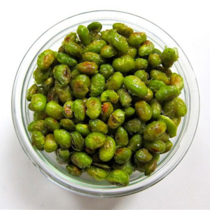 a glass bowl of crispy baked edamame on a white table