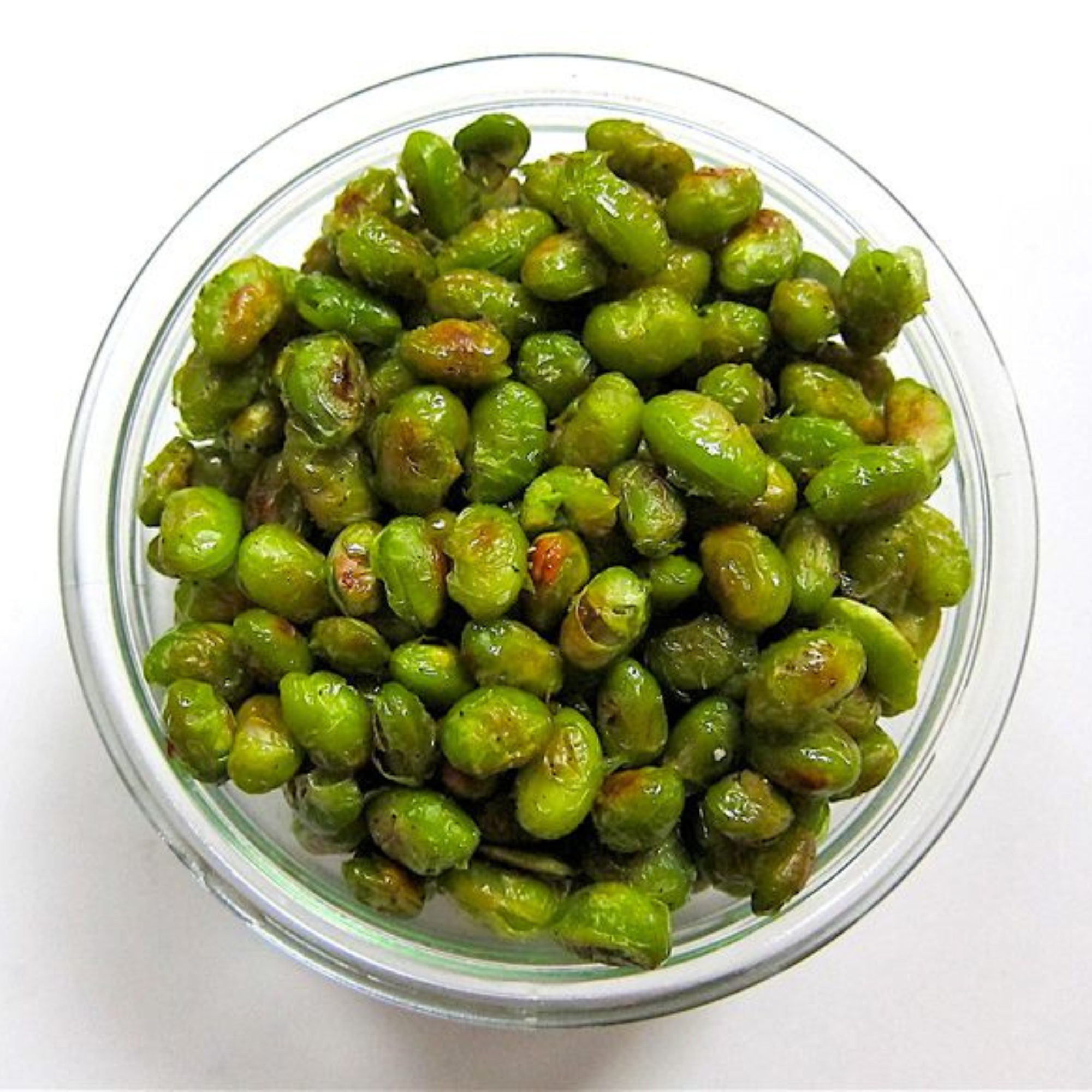 a glass bowl of crispy baked edamame on a white table