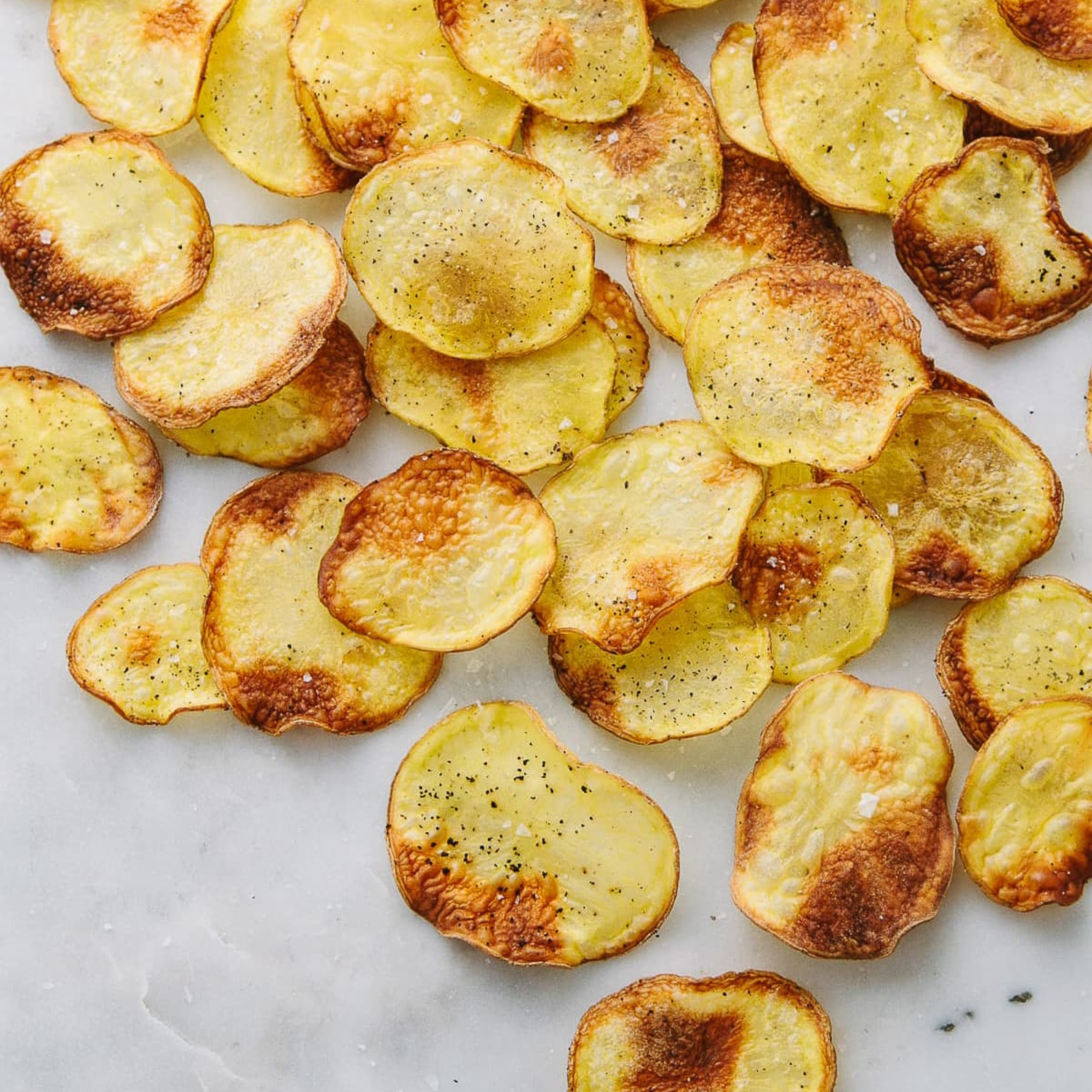 homemade baked potato chips layed out on a white marble countertop