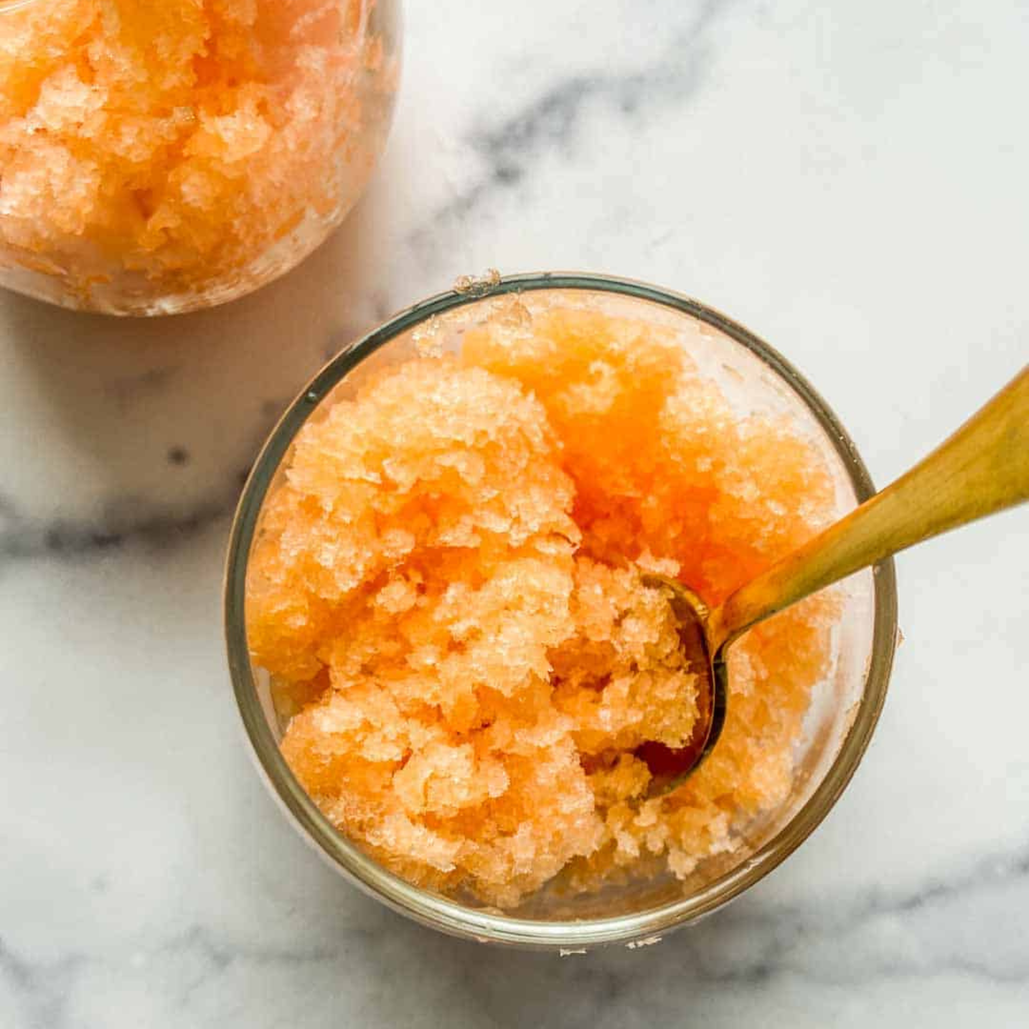 two glasses of cantaloupe granita with a gold spoon on a marble tabletop