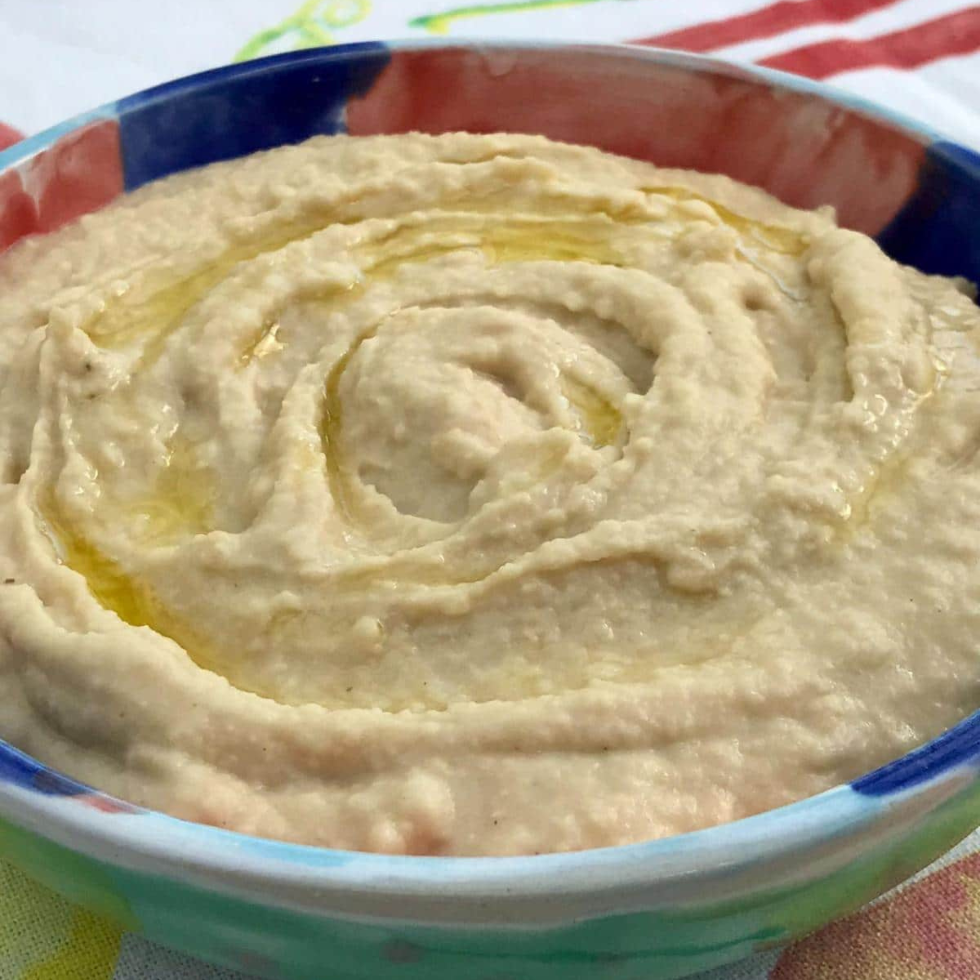 a big colorful bowl of two ingredient hummus on a coloful tablecloth 