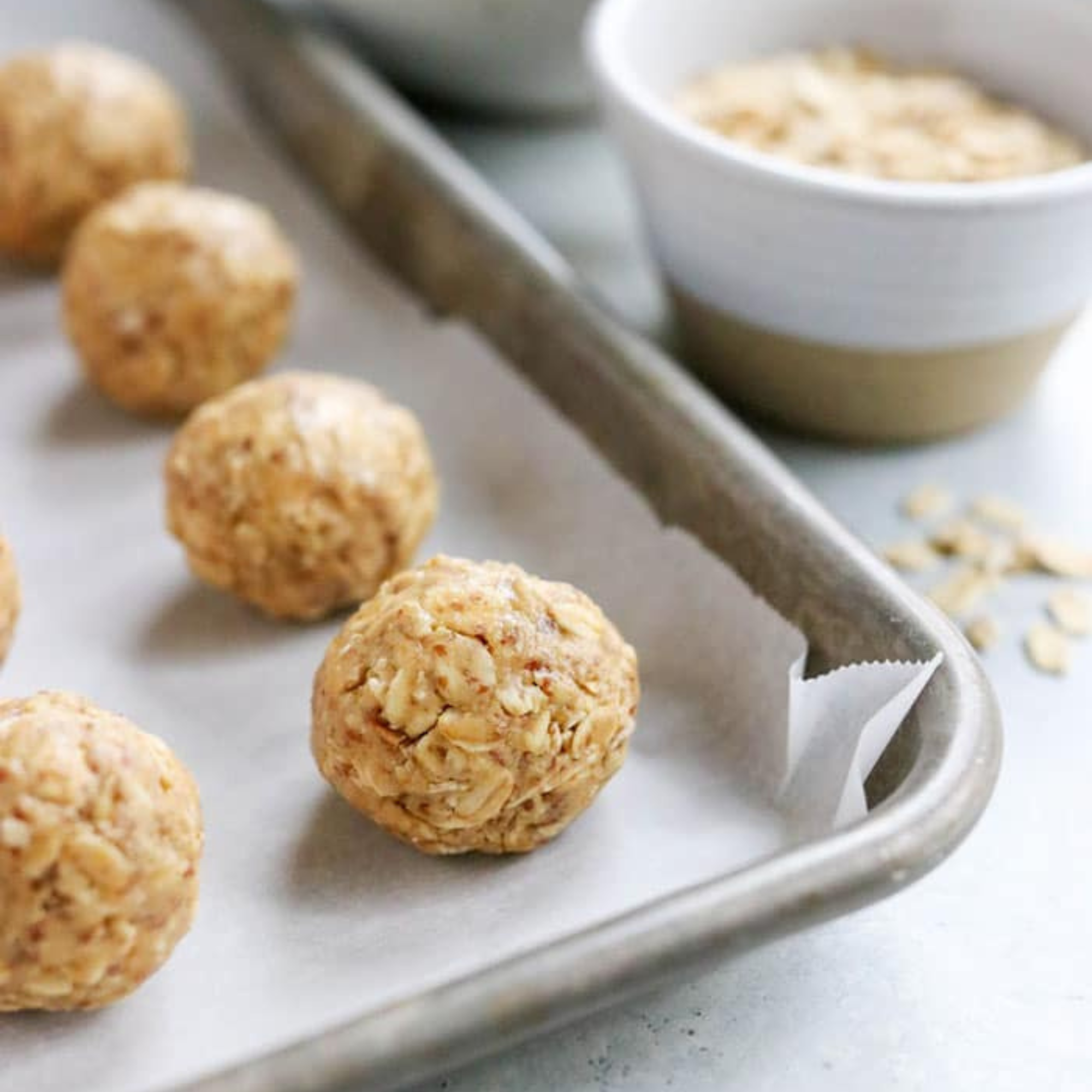 oat peanut butter balls on a parchment lined baking sheet with a bowl of oats behind it