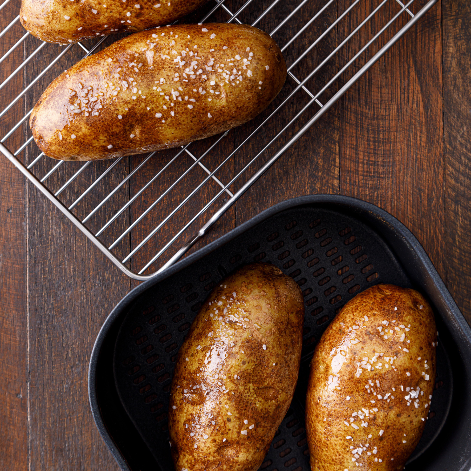 four baked potatoes sprinkles with salt, two are sitting in a skillet and two are on a cooling rack