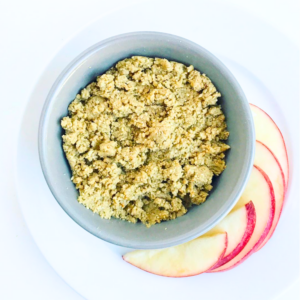 a bowl filled with homemade nutbutter on a white plate with apple slices on a white table