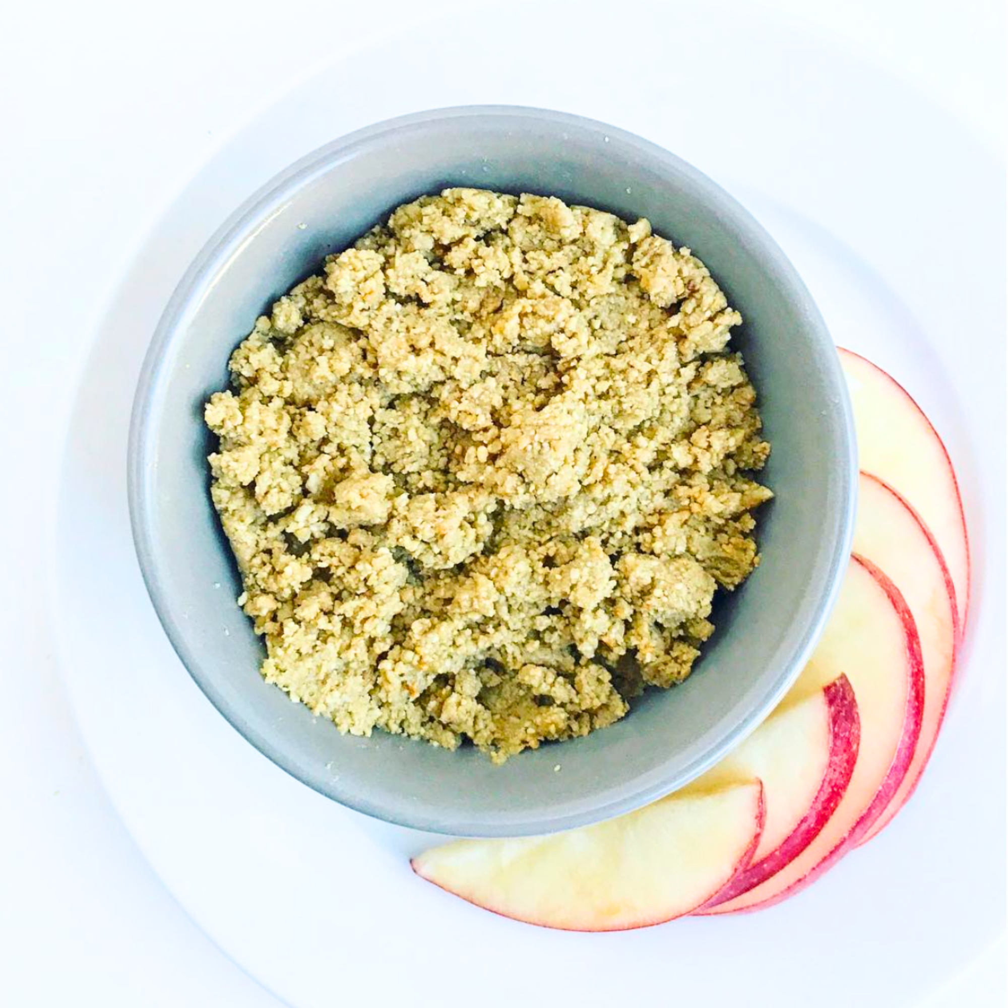 a bowl filled with homemade nutbutter on a white plate with apple slices on a white table