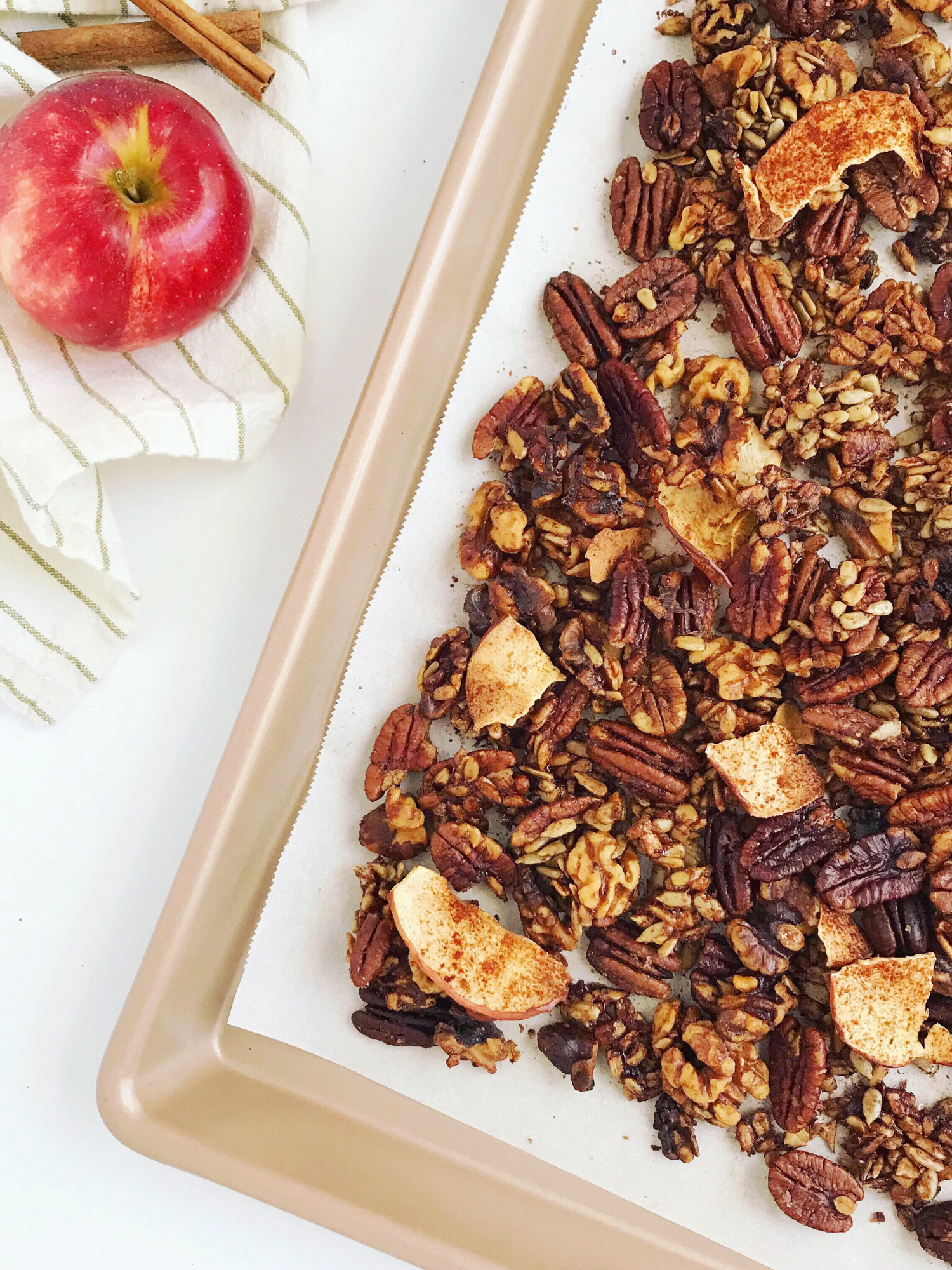 Grain-free cinnamon apple granola on a baking sheet with an apple and cinnamon sticks in the background.