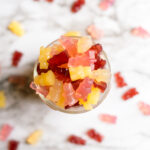 a small jar full of colorful vegan gummy bears with some spilled out and around the jar