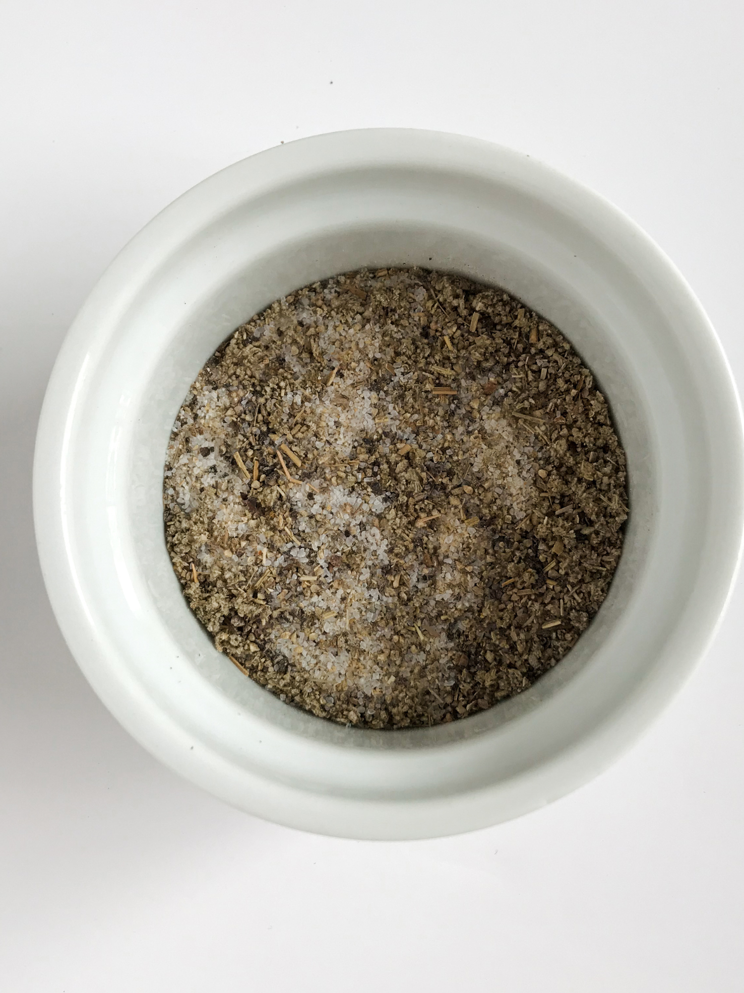 a small white bowl filled with spices like Dried Oregano, Rubbed Sage, Celery Salt, Dried Marjoram, Salt, Onion and Garlic Powder mixed together