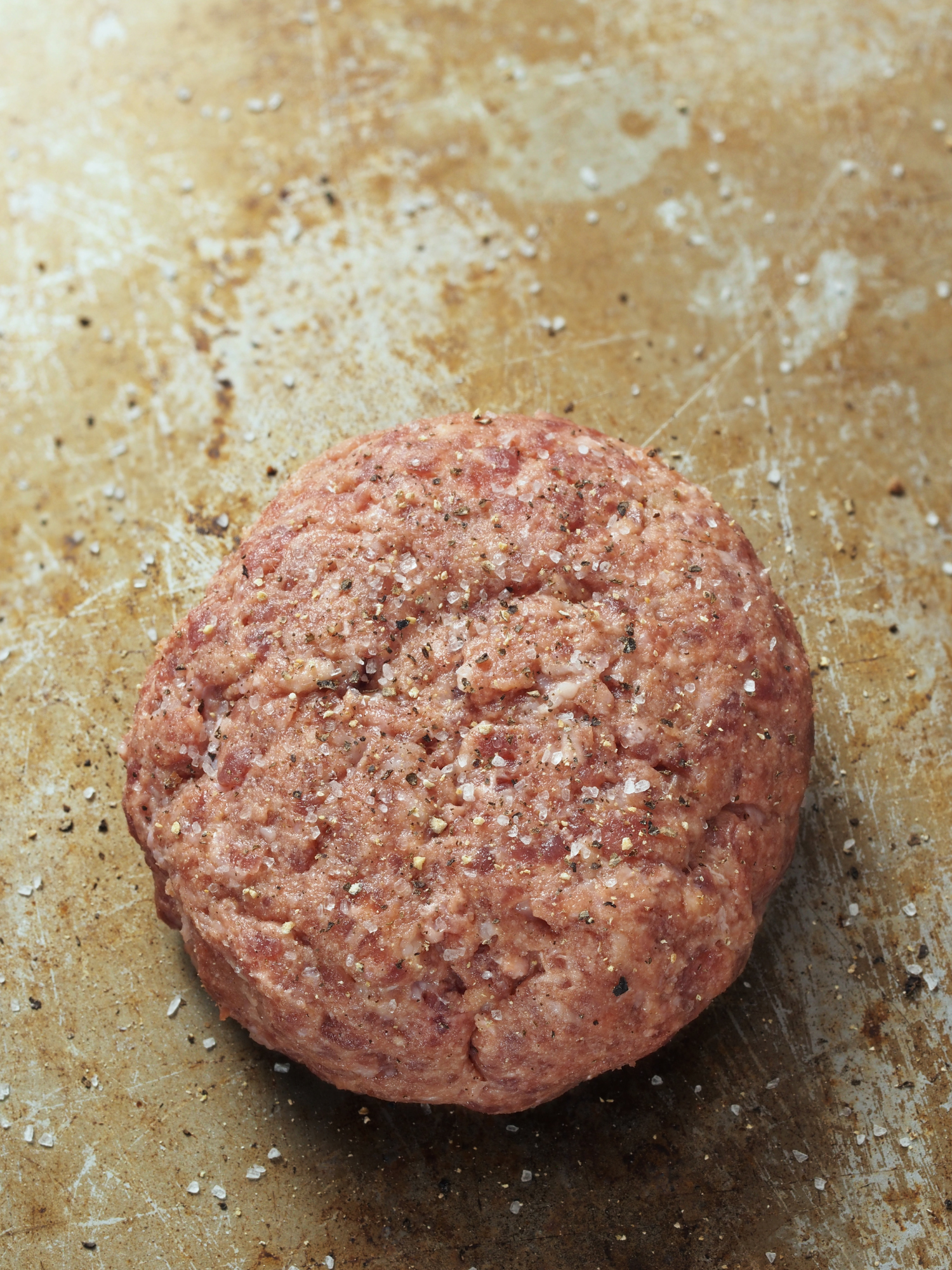 a raw hamburger patty sprinkled with our NO Heartburn Hamburger Seasoning sitting on a baking sheet