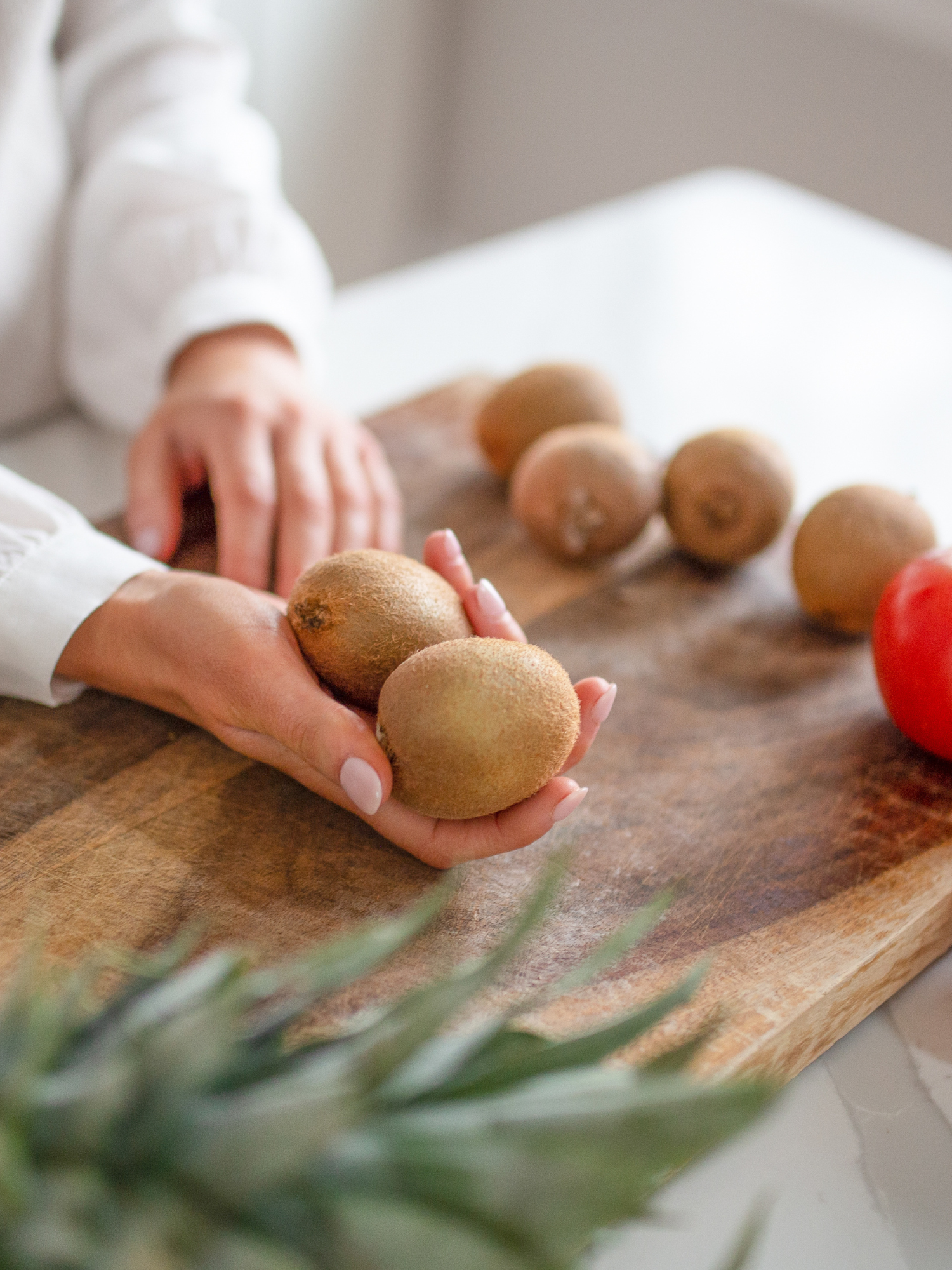 a cutting board on a white kitchen counter with kiwis and a dietitians hands holding out two kiwis