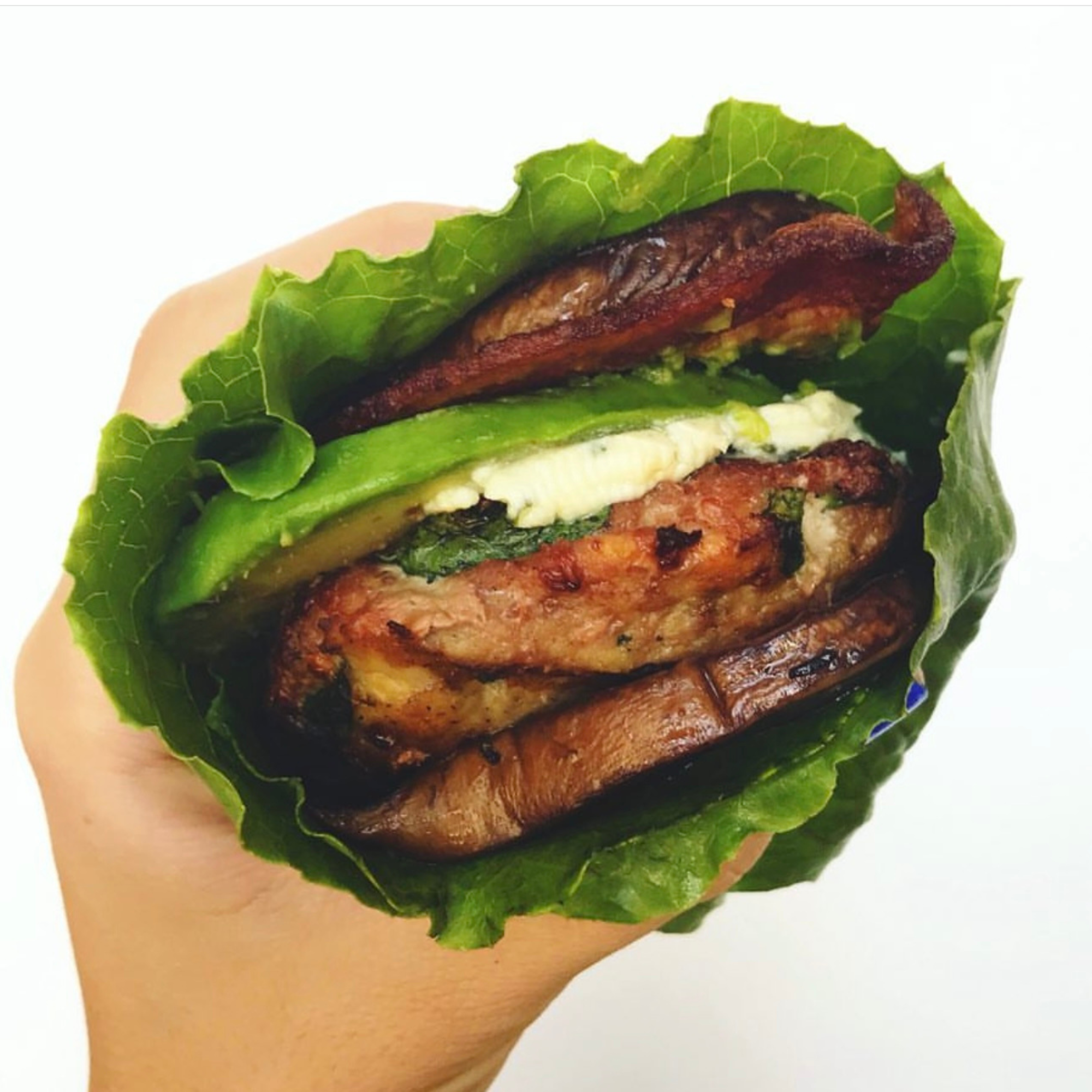 a hand holding a loaded lettuce wrapped turkey burger that is stuffed with sautéed portobello mushrooms, bacon, avocado all wrapped up in crunchy romaine 