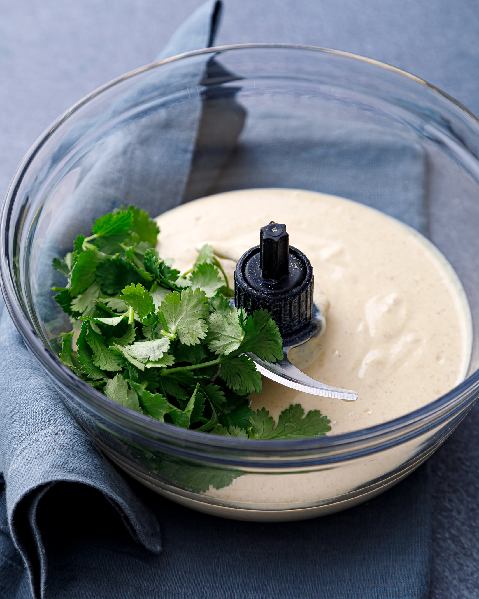 a glass bowl full of creamy and delicious tofu queso with a handful of fresh cilantro on top