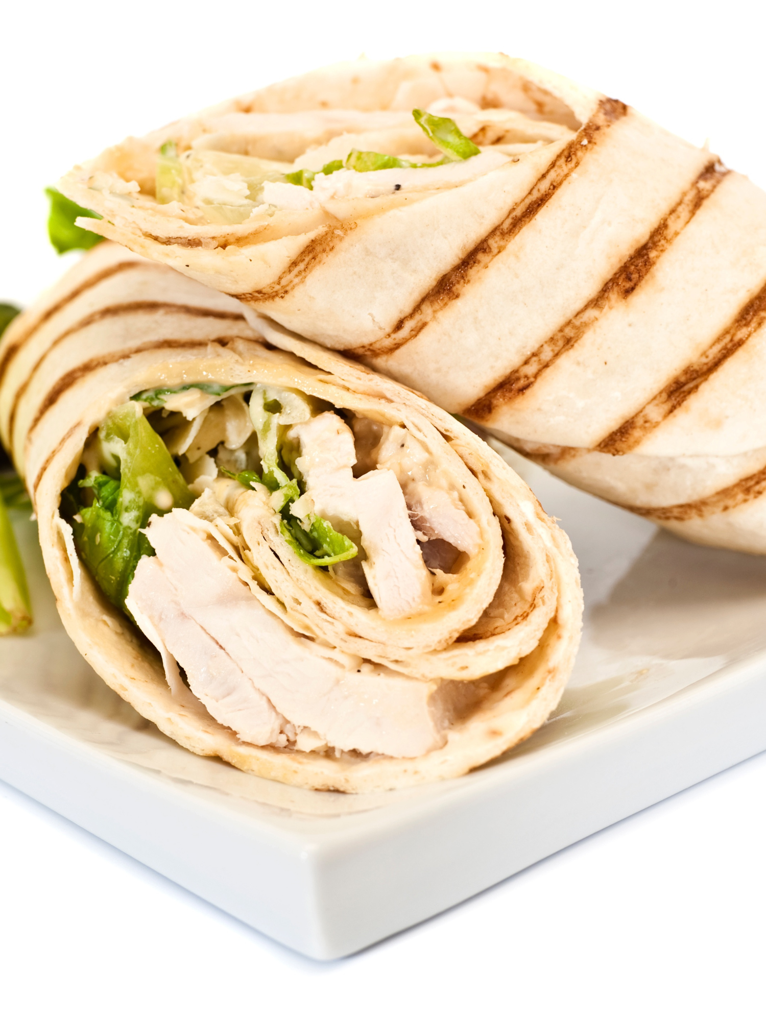 a grilled wrap filled with turkey and lettuce cut in half and placed on a white marble serving dish