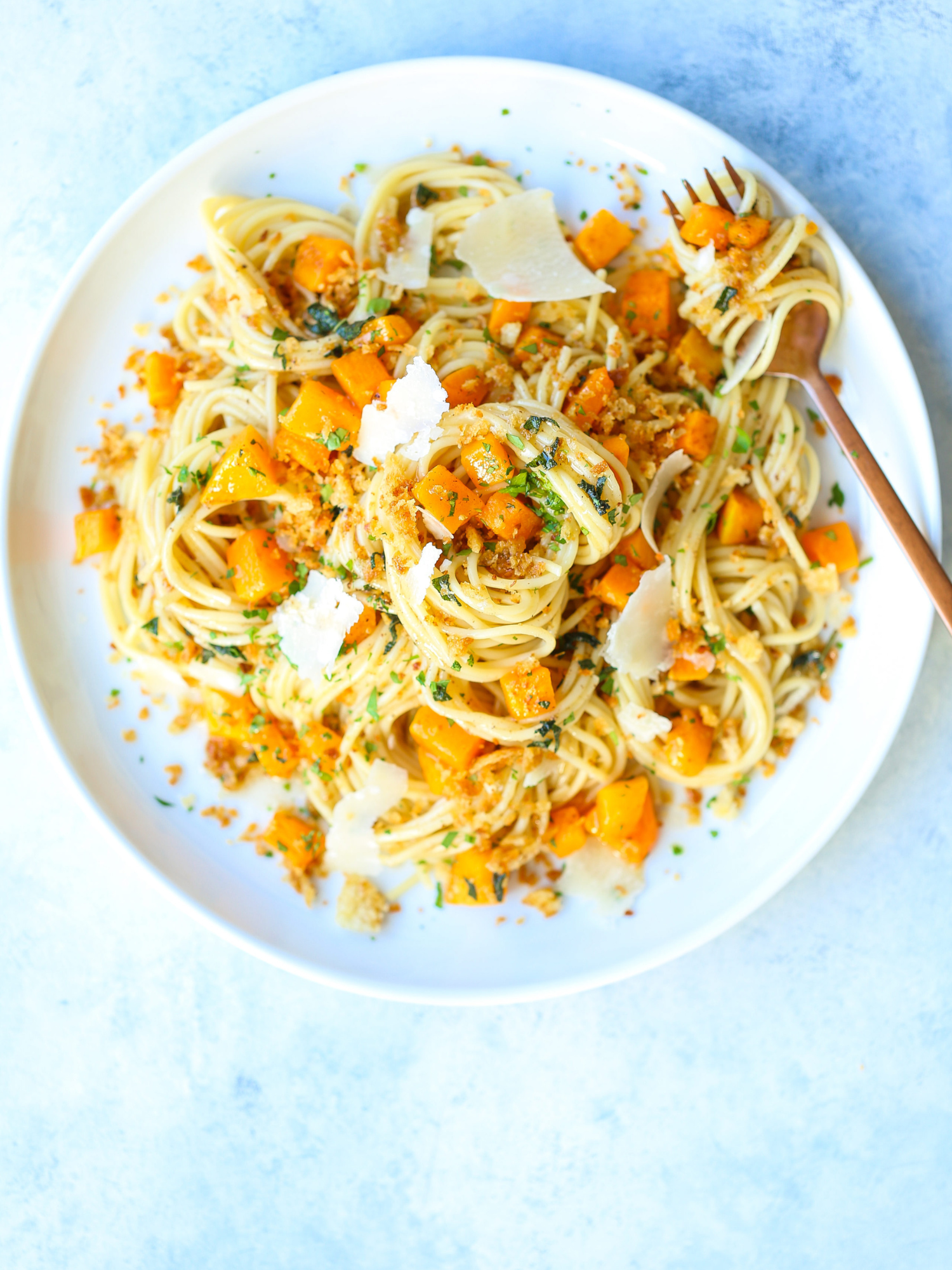 a white plate of brown butter butternut squash pasta with a fork on a white/blue table