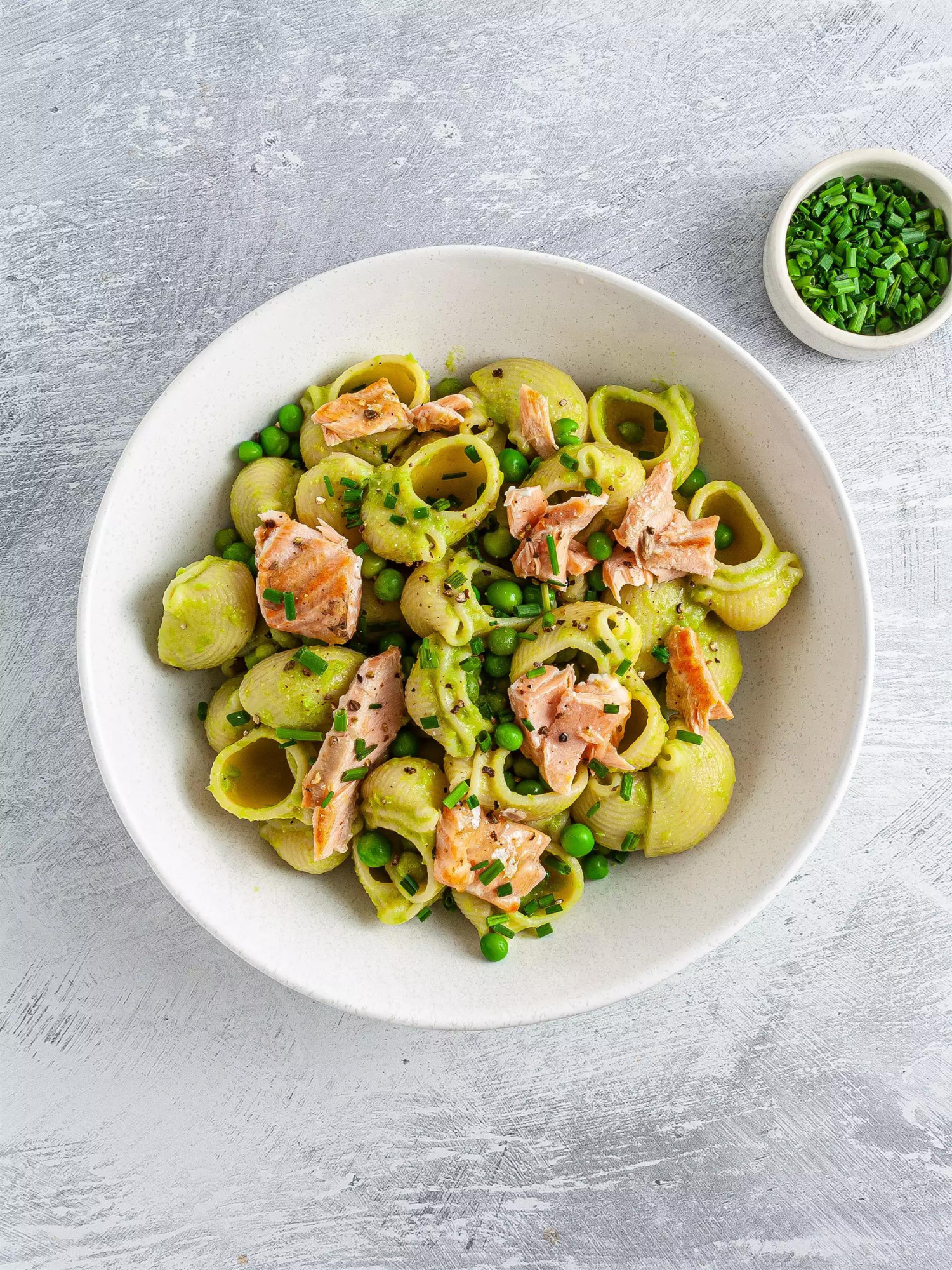 a white bowl of dairy free salmon pasta with peas and a small white bowl of peas sitting to the side of it/