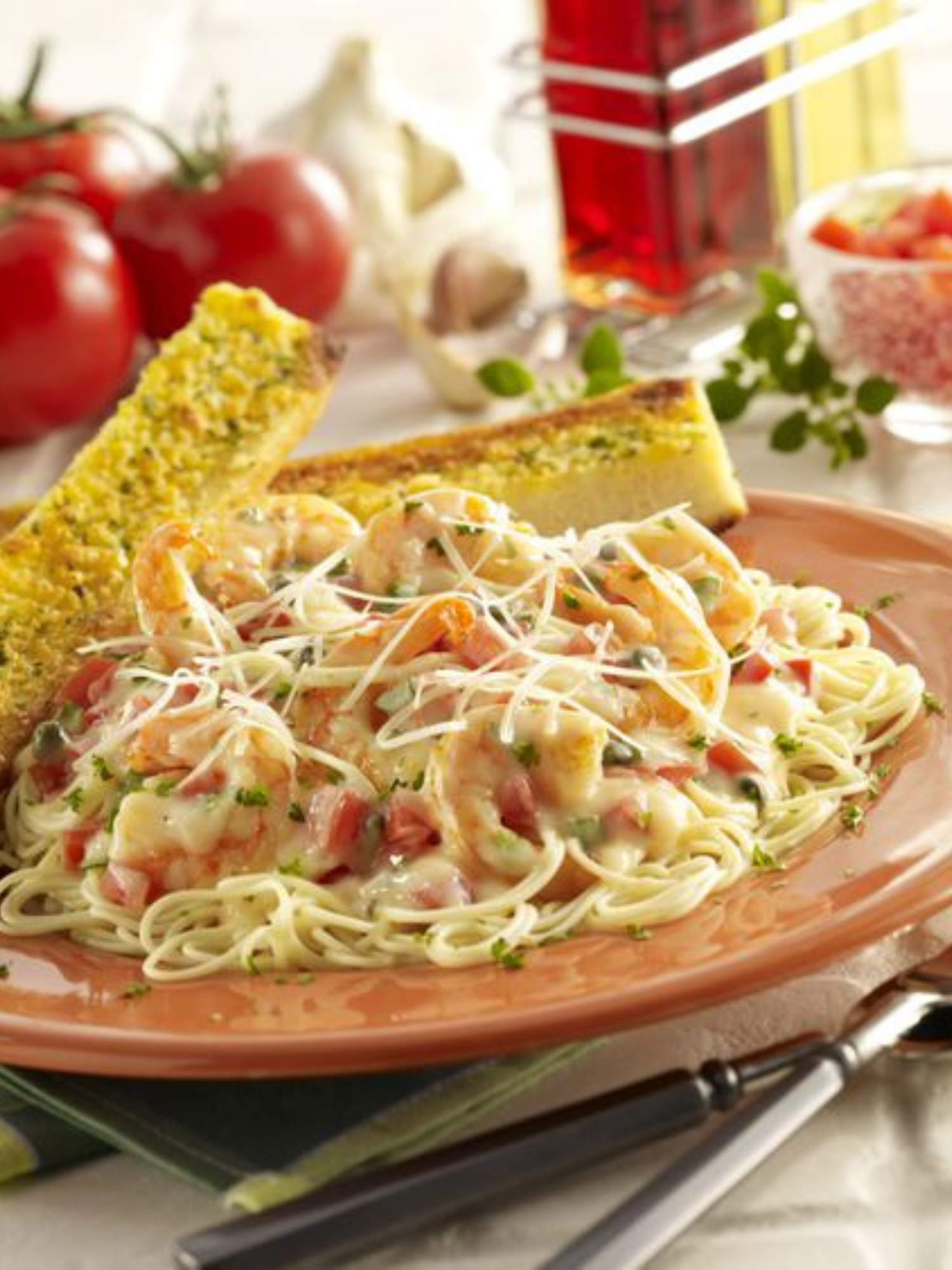 a plate of low fat shrimp pasta with two pieces of french bread and tomatoes in the background