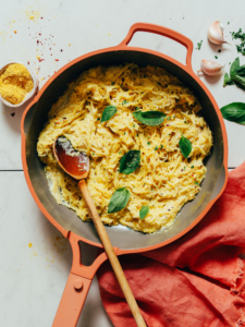 a red skillet of one pot spaghetti squash alfredo topped with fresh basil leaves and a wooden spoon