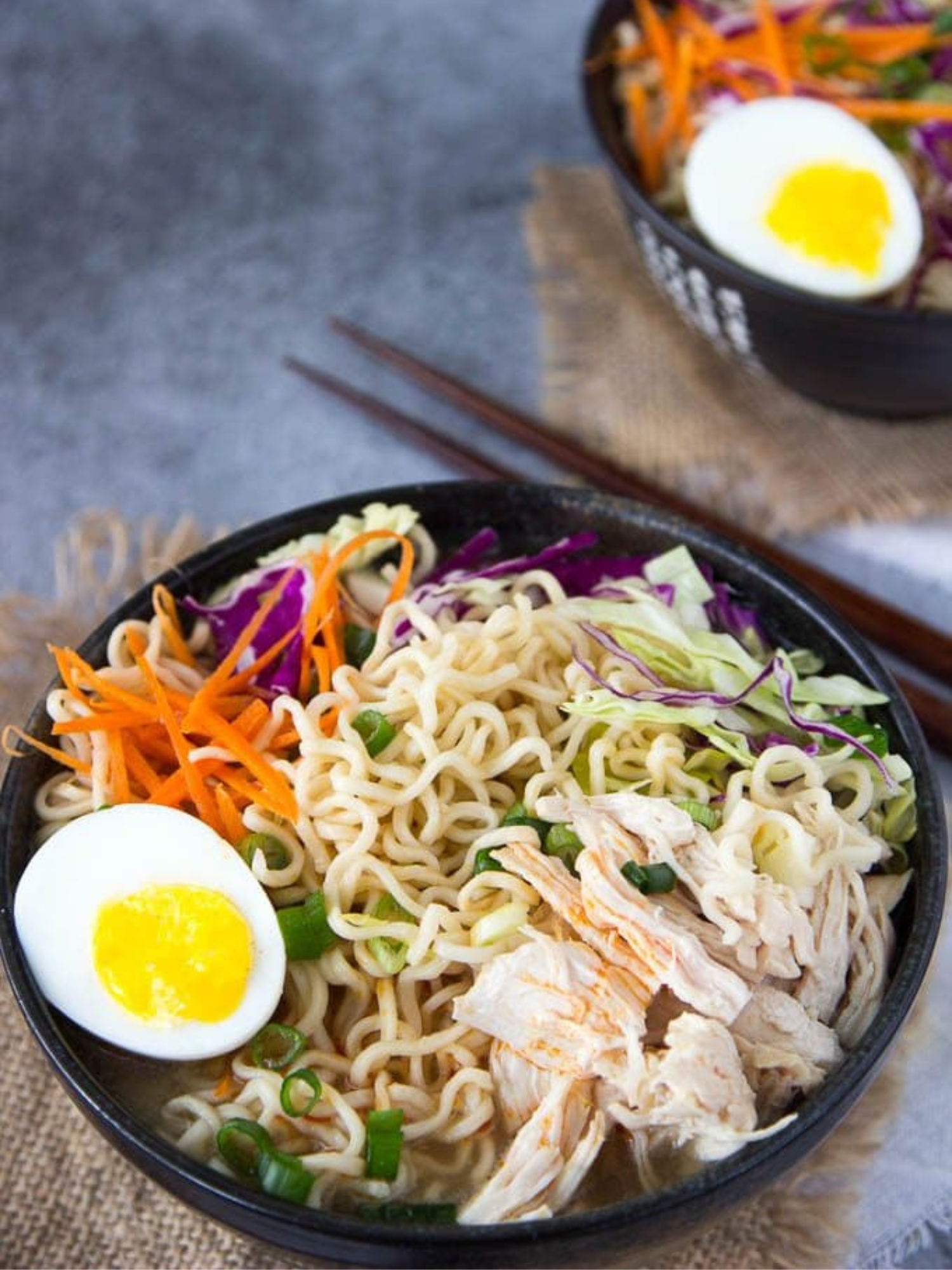 a black bowl of healthy chicken ramen with chopsticks and a second bowl behind it.